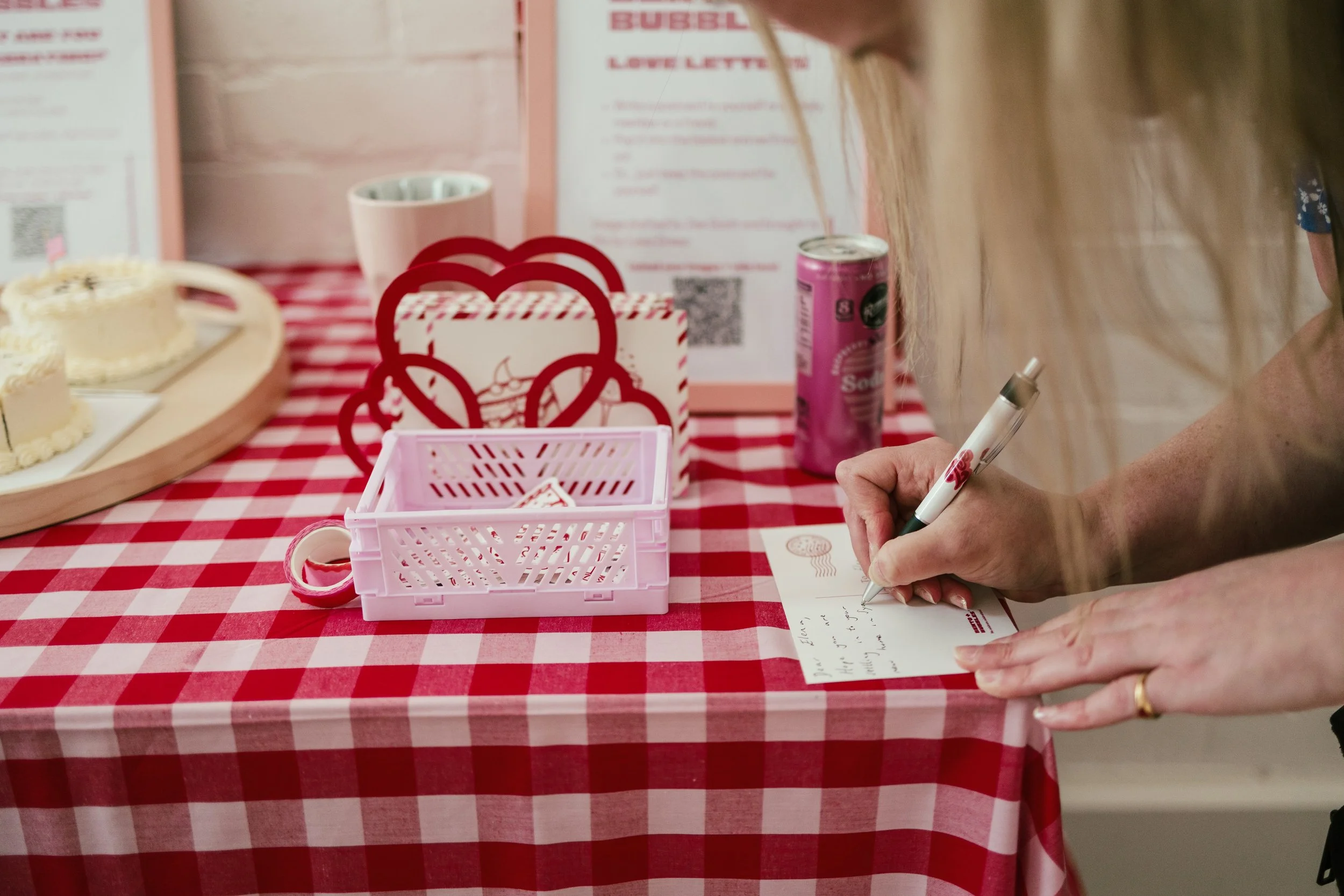 Person writing on a card at a table with cupcakes and pink decorations at a bubble tea shop.