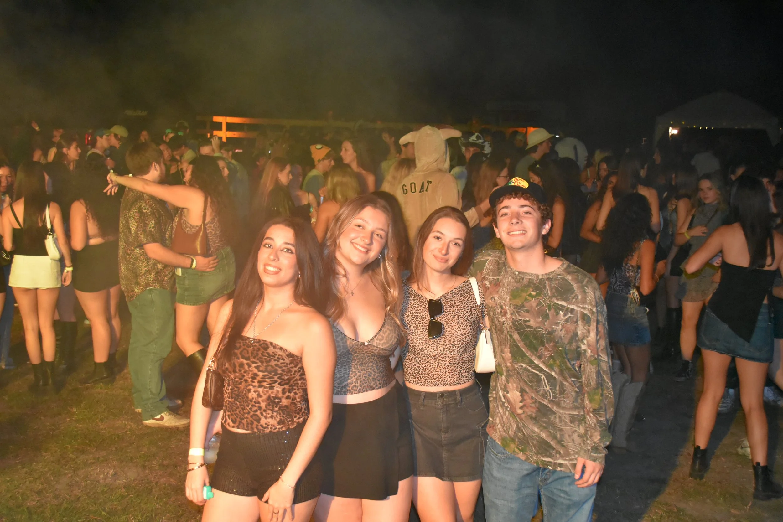 Group of four young people posing at a crowded outdoor night event or concert.