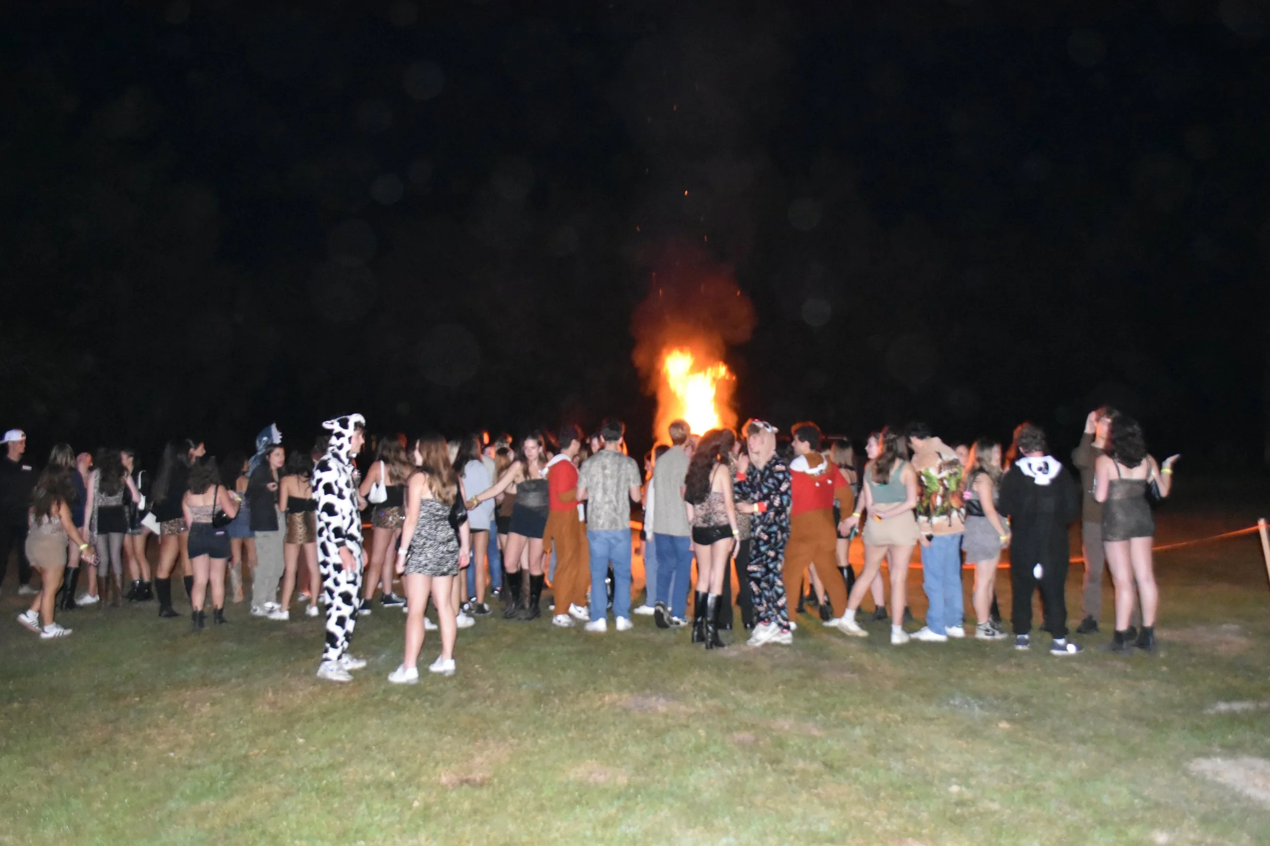 Group of people participating in a nighttime bonfire party outdoors.