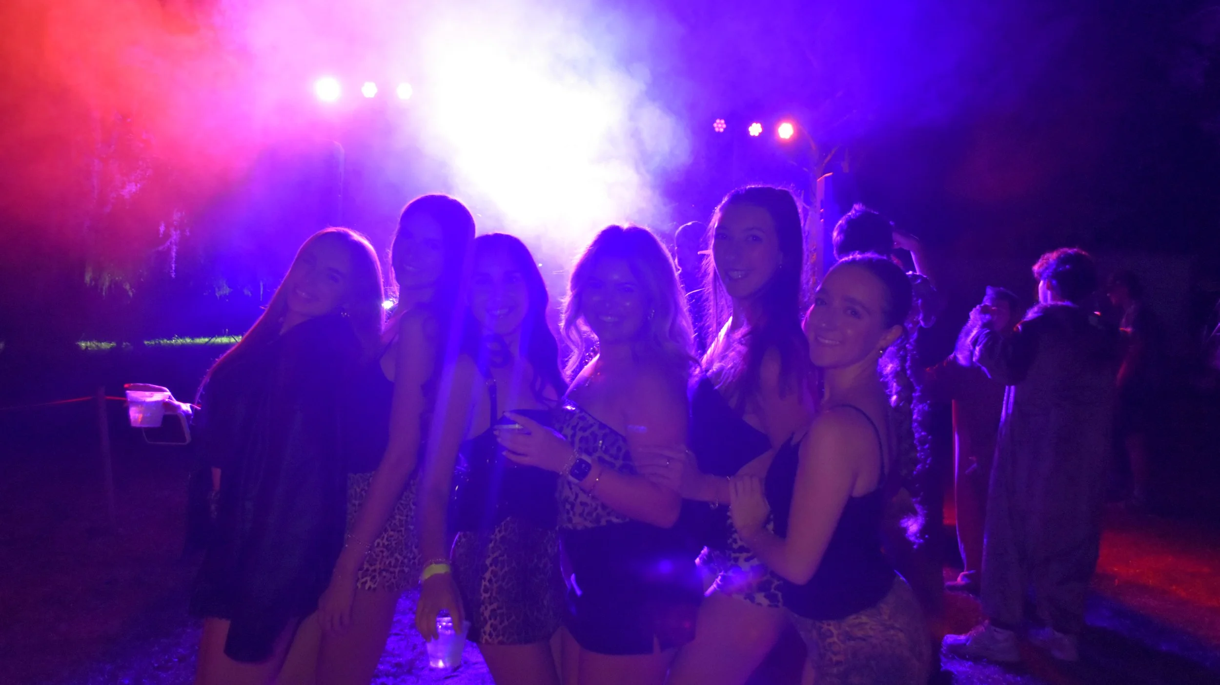 Group of women smiling at a nighttime outdoor event with colorful stage lighting.