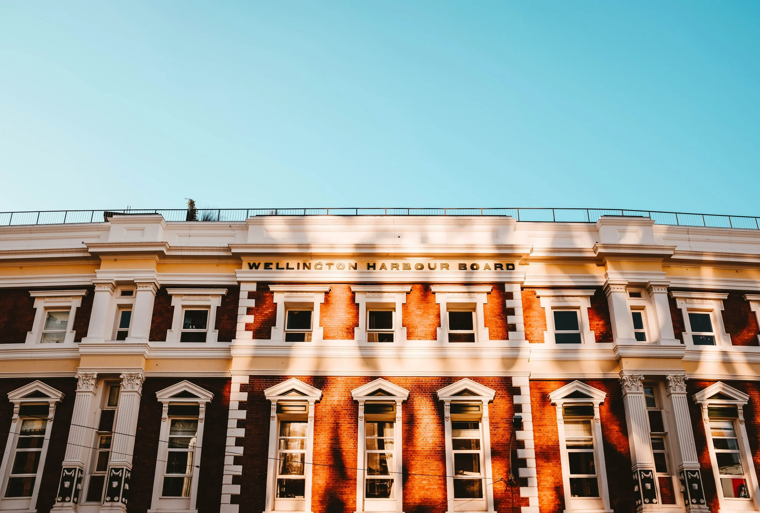A historic building with white and red brick facade, multiple windows, and decorative architectural details, with a clear blue sky overhead.
