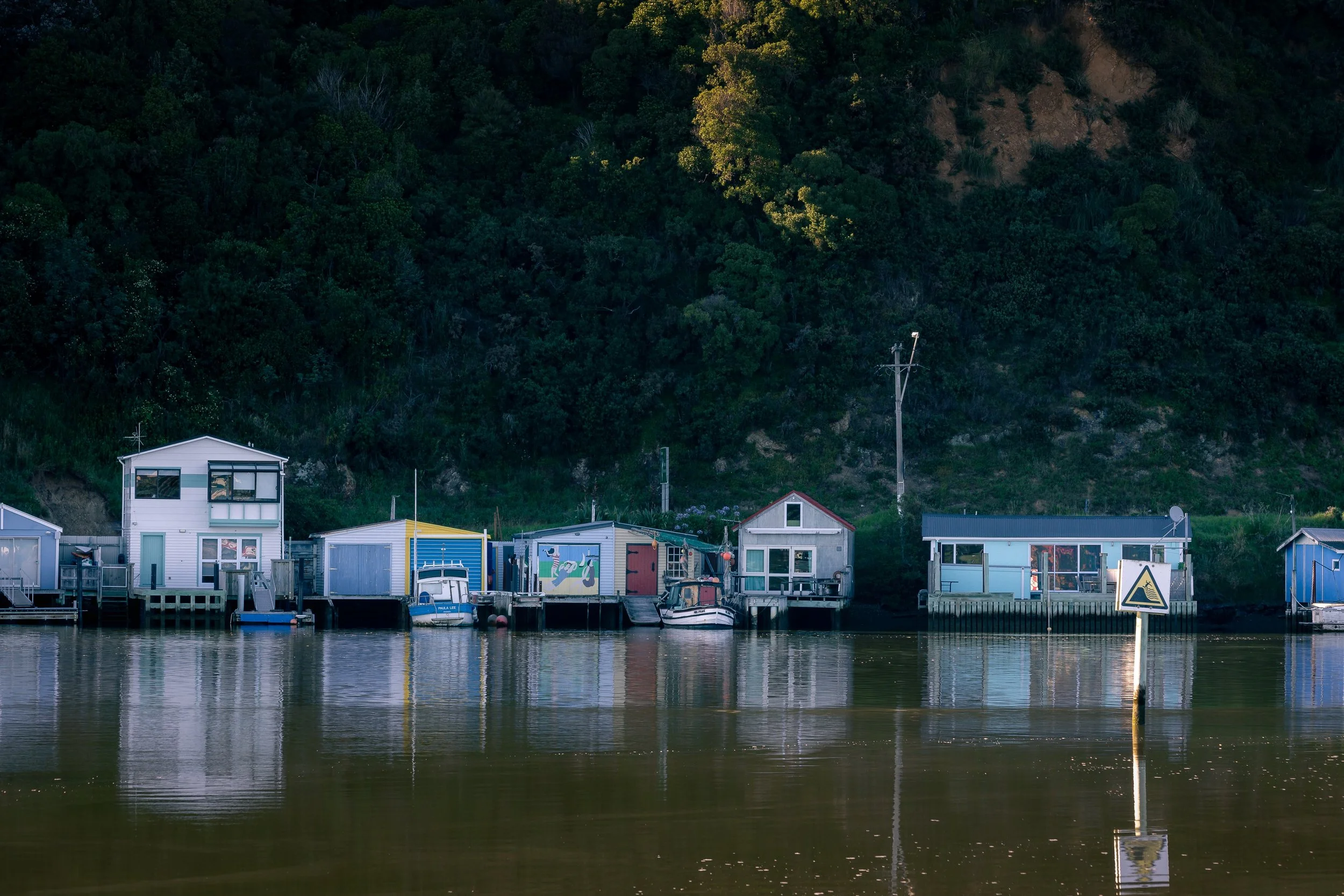 Colorful floating houses and boats along a waterway with lush green hillside in the background.
