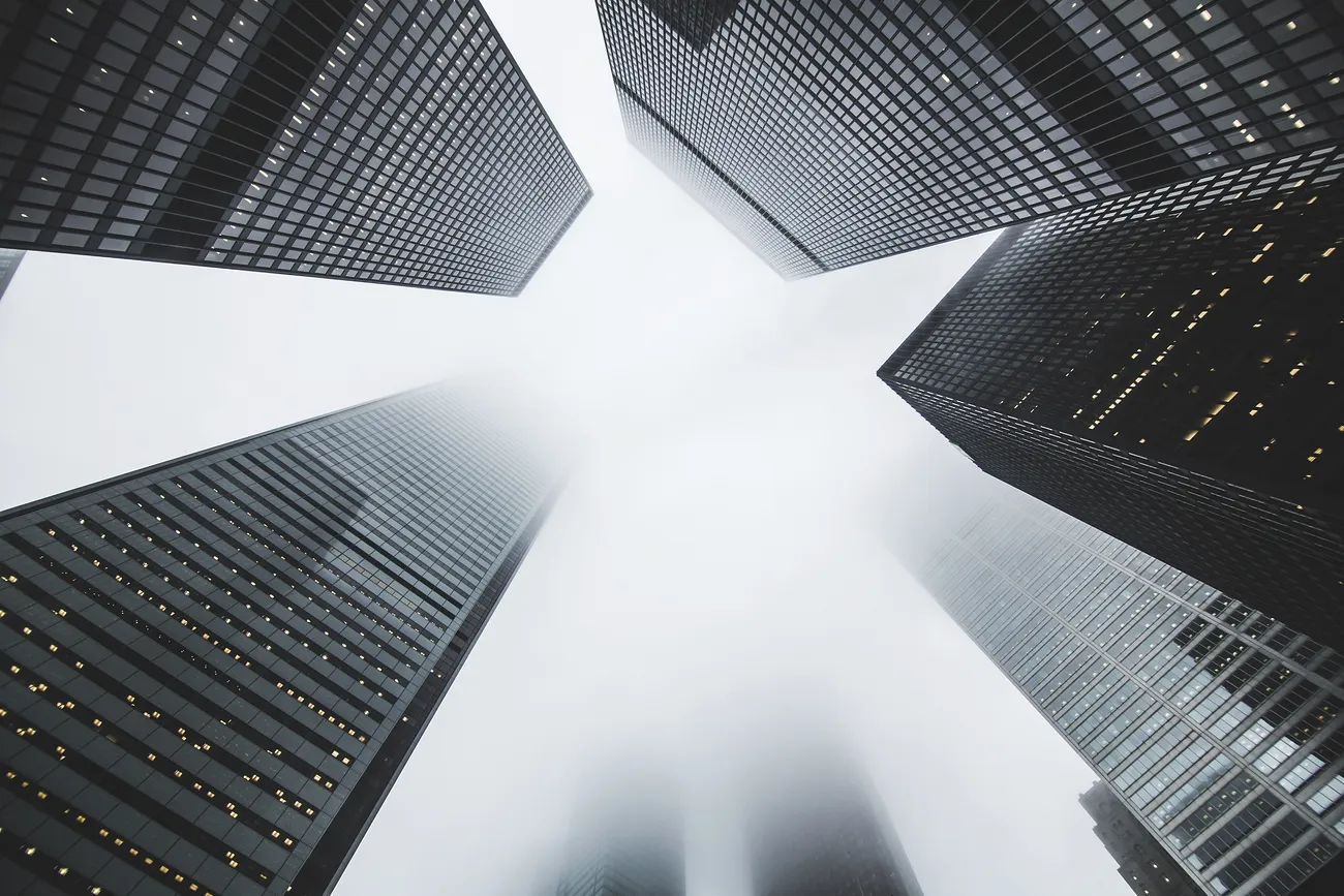 Looking up at tall modern skyscrapers in foggy city.