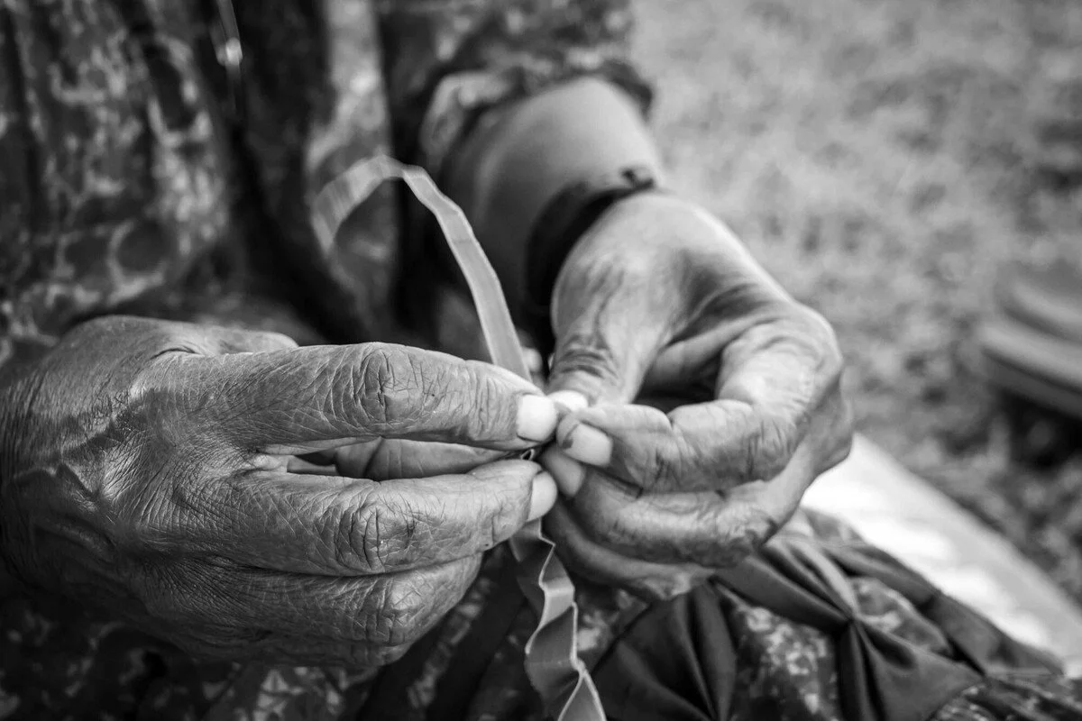 Close-up of elderly person's hands threading a needle, black-and-white photo.