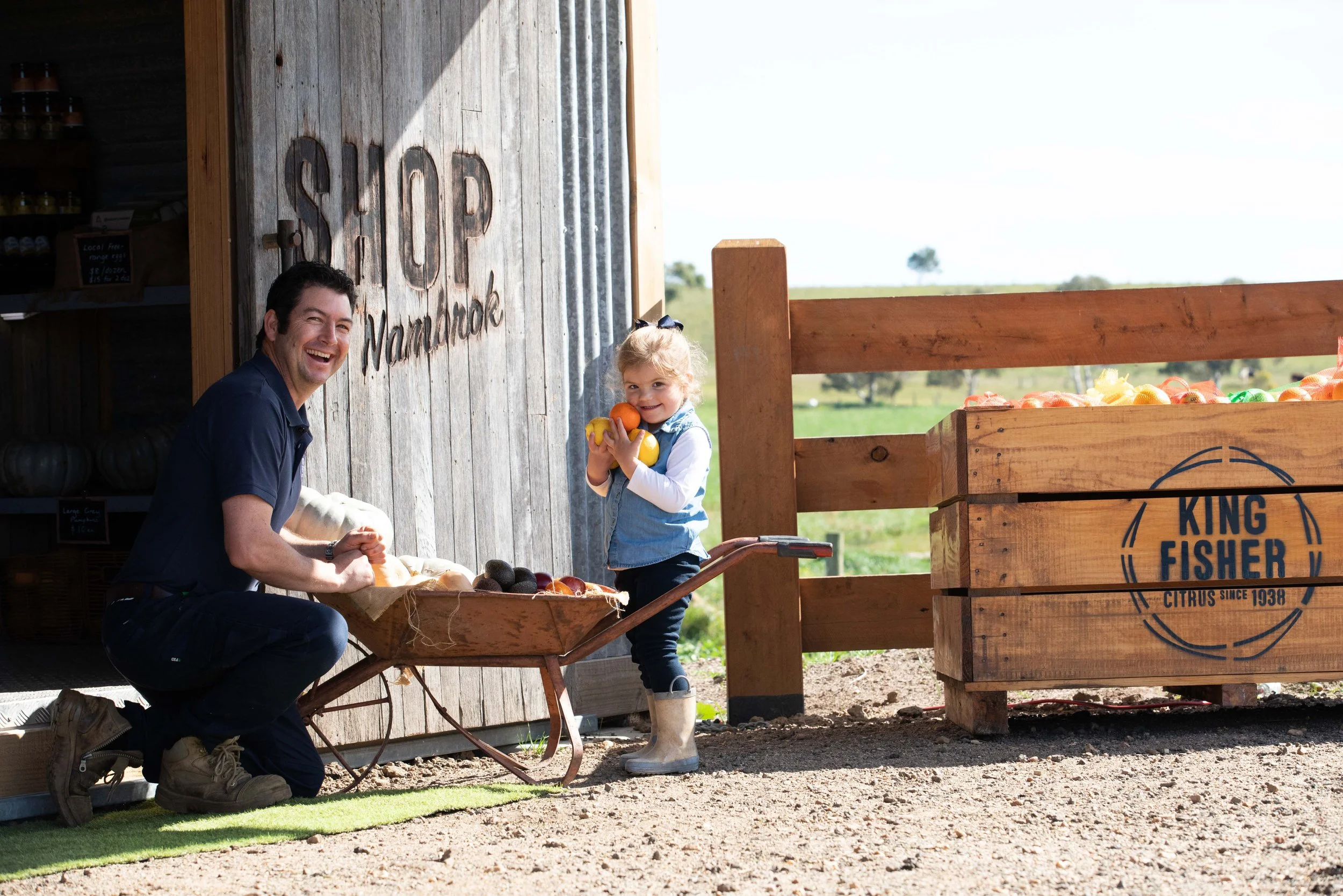 Lynton Fisher with daughter, both smiling with a wheelbarrow of fresh produce at their farm in Gippsland.