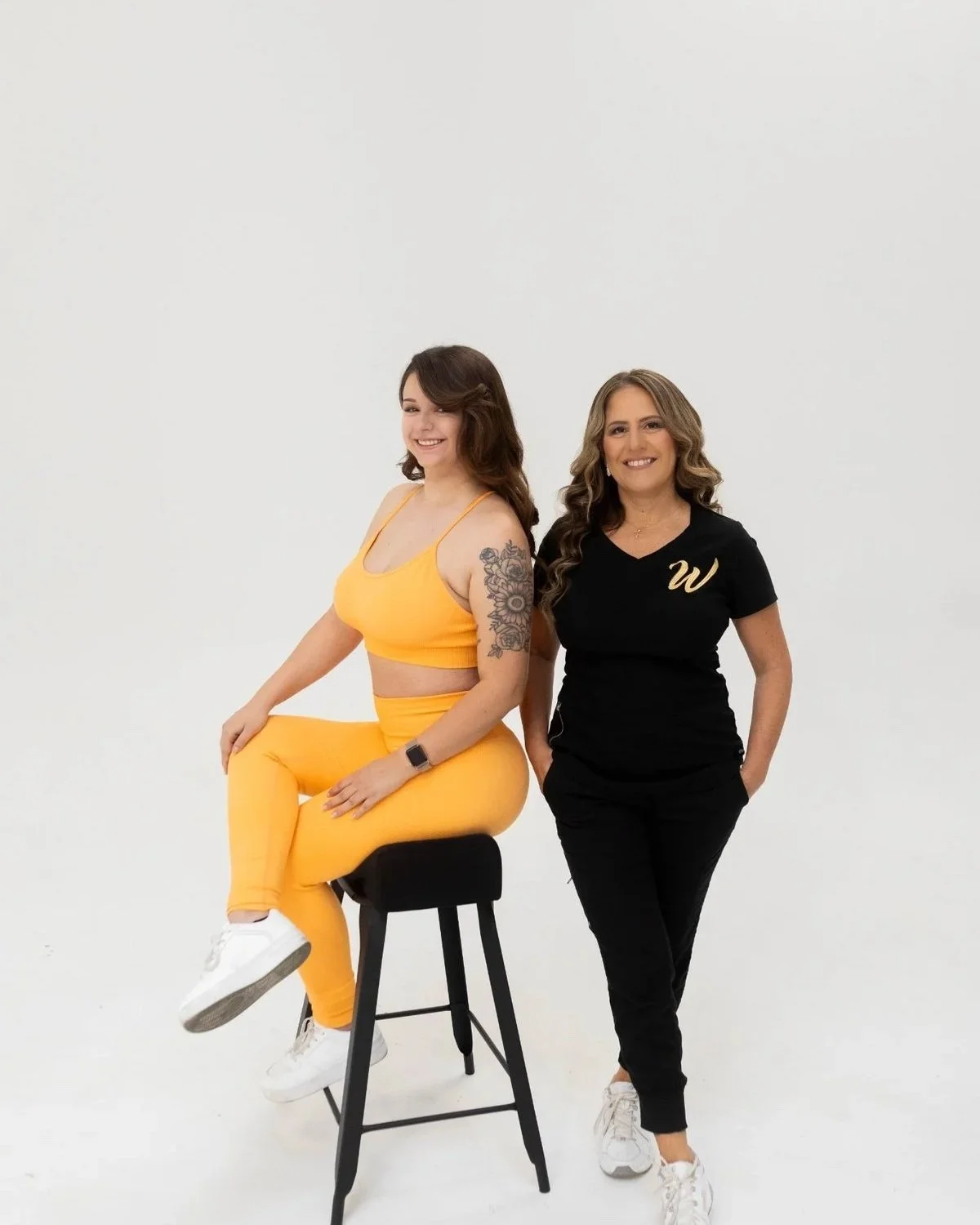 Monica Skalsky, founder of Wrthit and Peaches by Wrthit, wearing black scrubs and a model wearing orange workout pants and top sitting on The Bellini BBL Pillow.