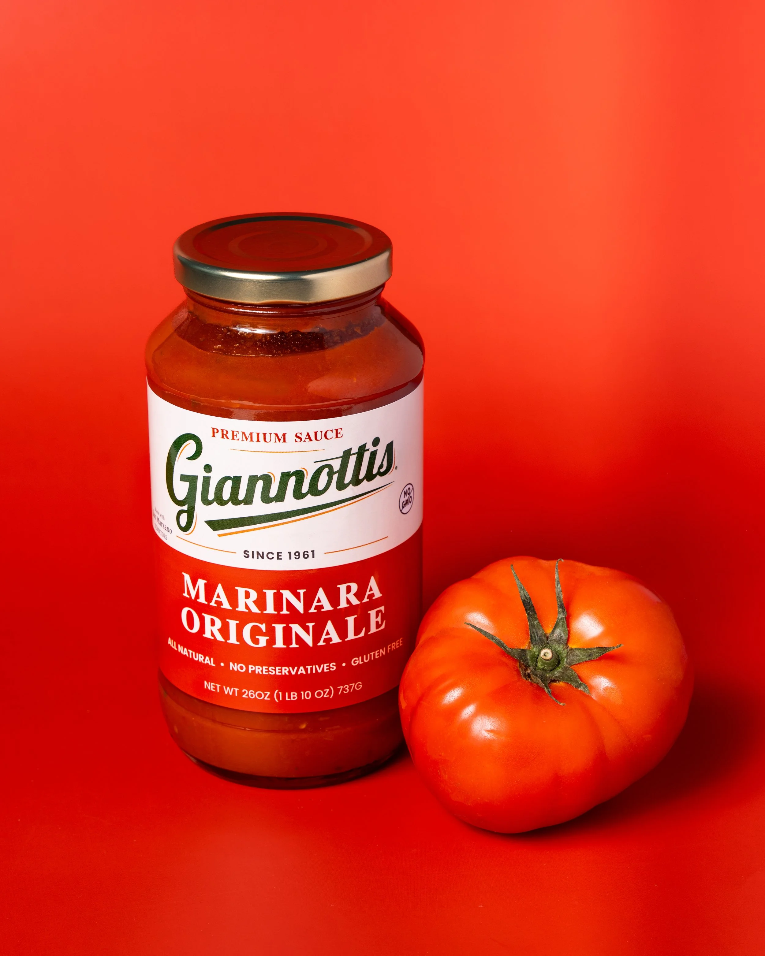 Giannotti’s Marinara Originale sauce jar beside a tomato against a red background