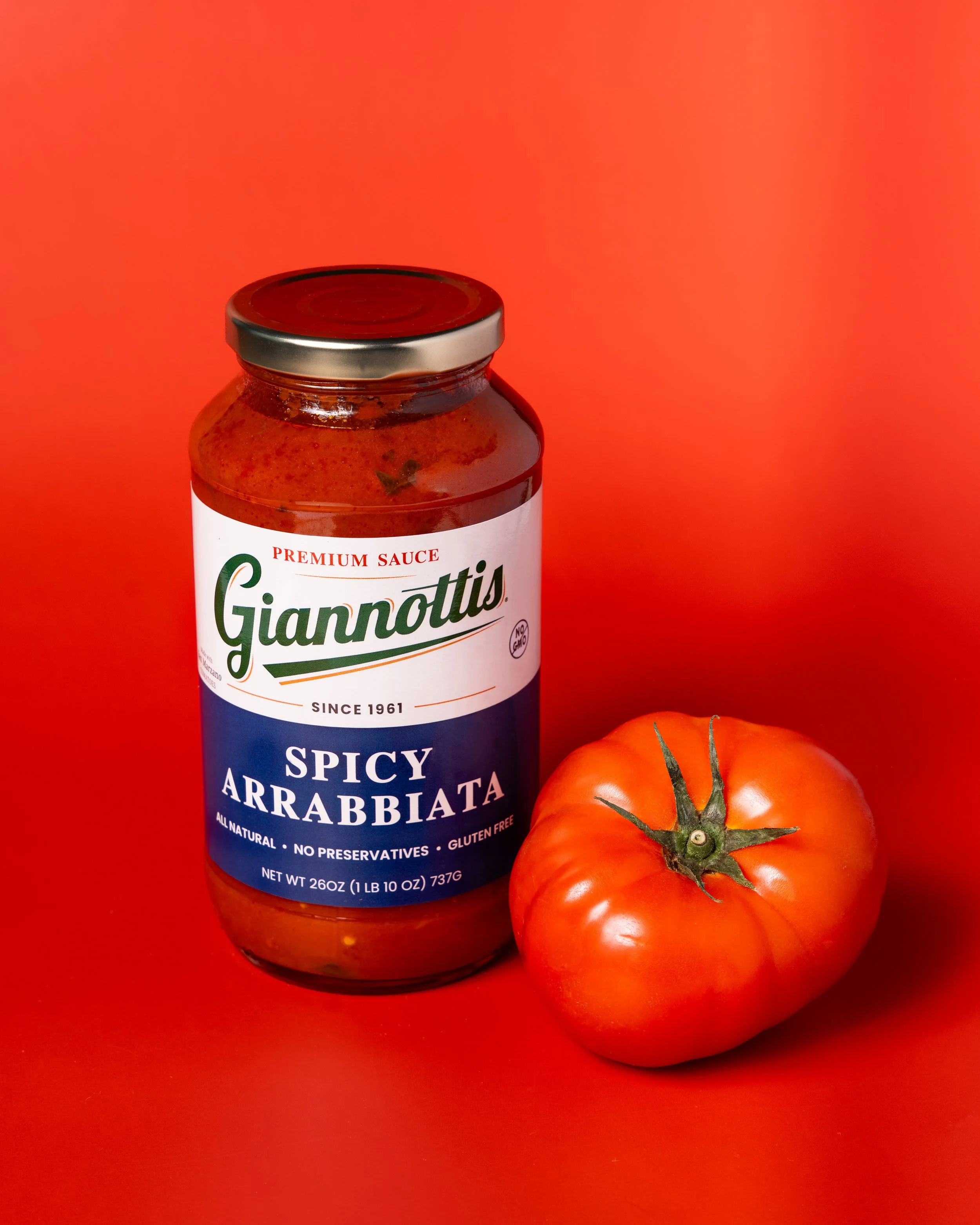 Giannotti’s Spicy Arrabbiata sauce jar beside a tomato against a red background