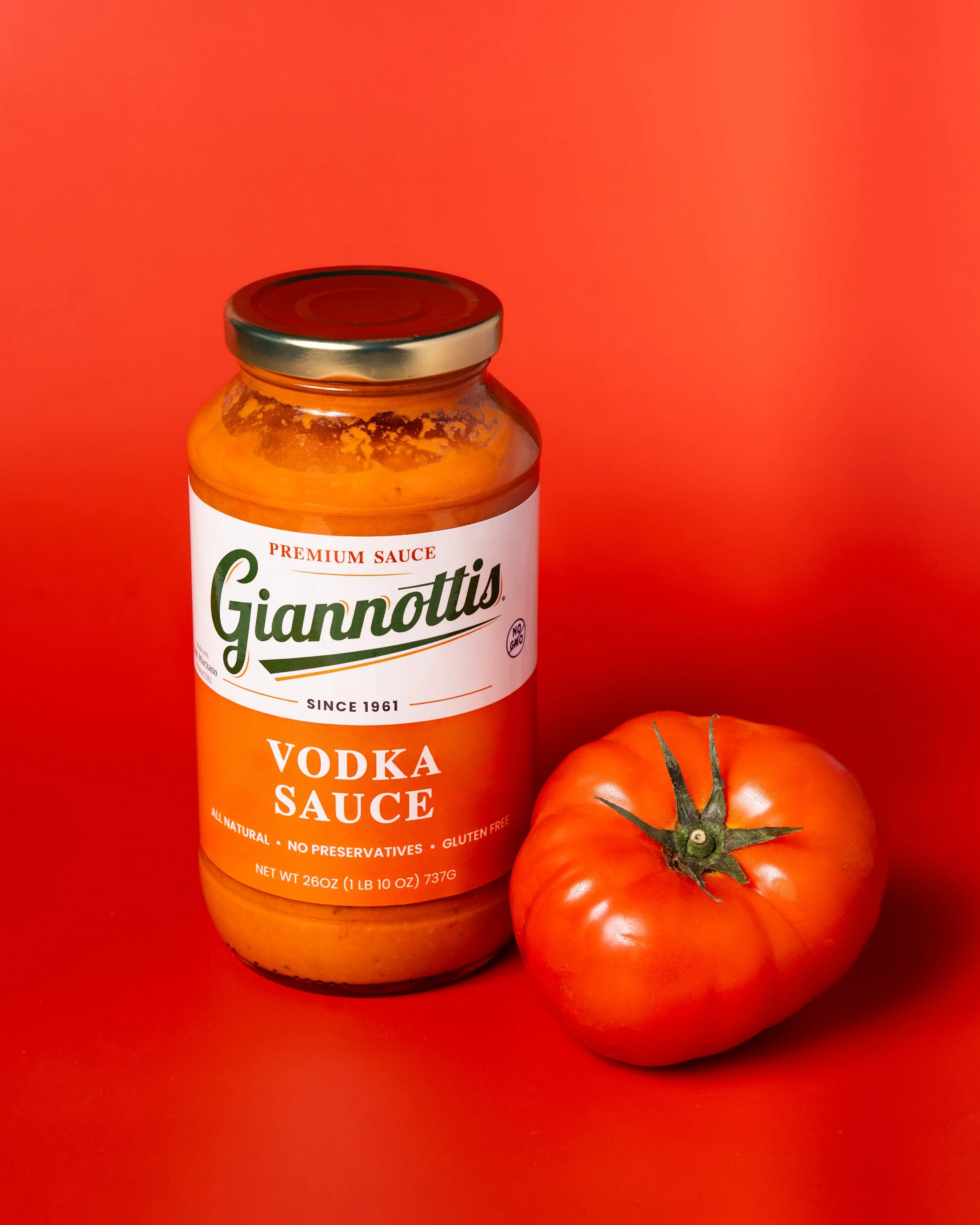 Giannotti’s Vodka Sauce jar beside a tomato against a red background