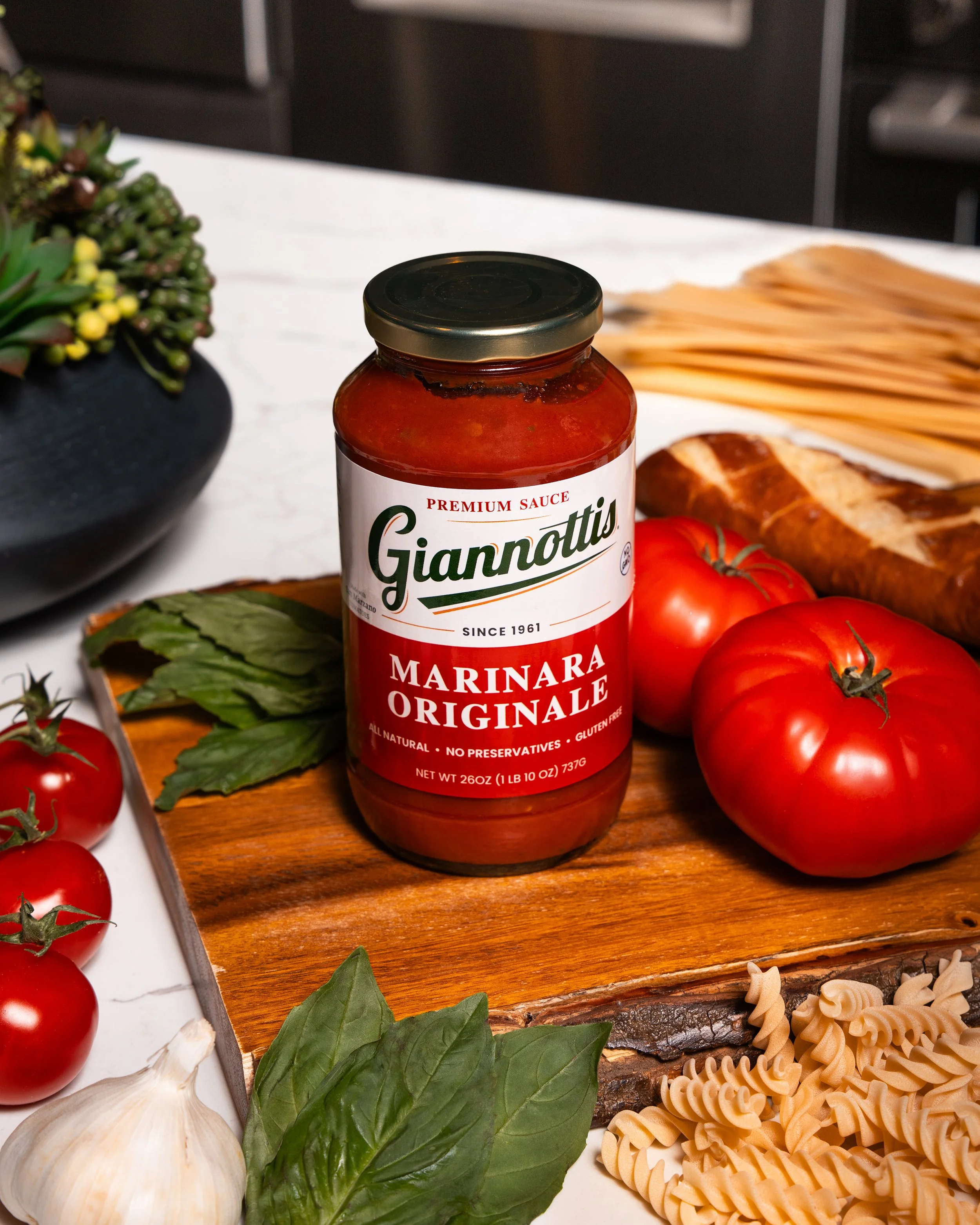 Giannotti’s Marinara Originale sauce jar with tomatoes, basil and pasta on a kitchen board