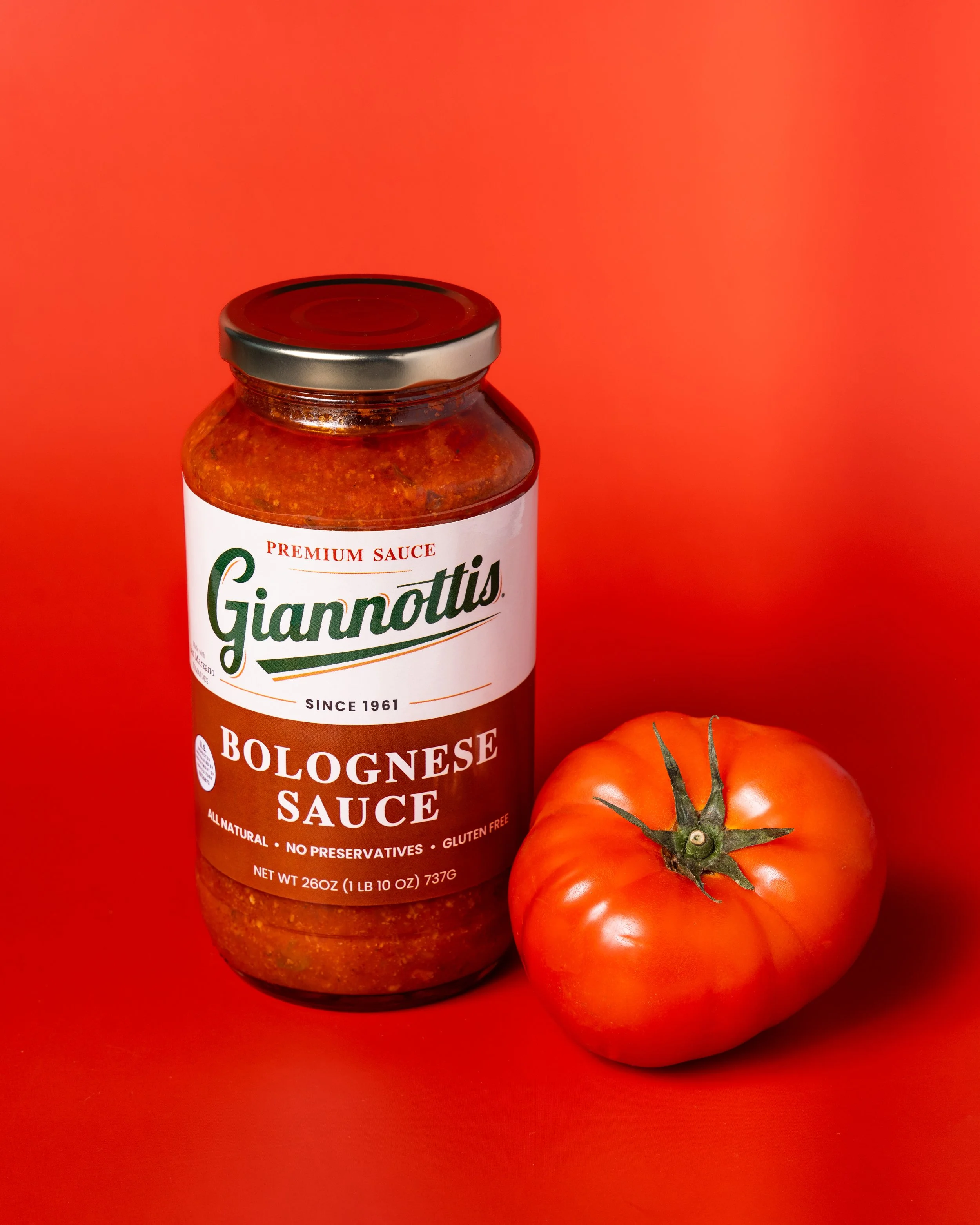 Giannotti’s Bolognese Sauce jar beside a tomato against a red background