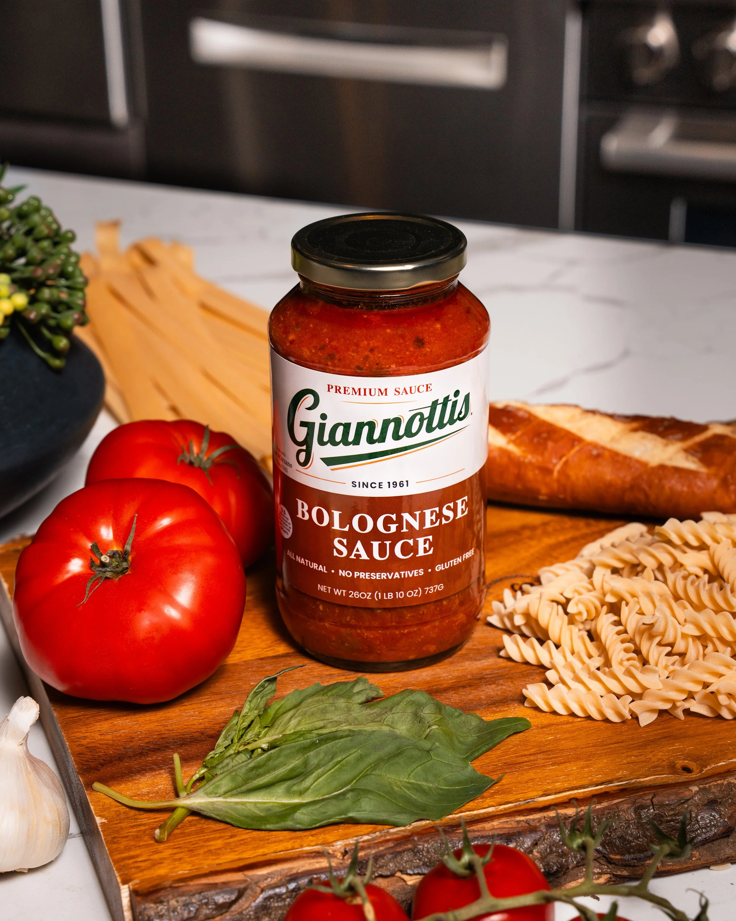Giannotti’s Bolognese Sauce jar with tomatoes, basil, bread and pasta on a kitchen board