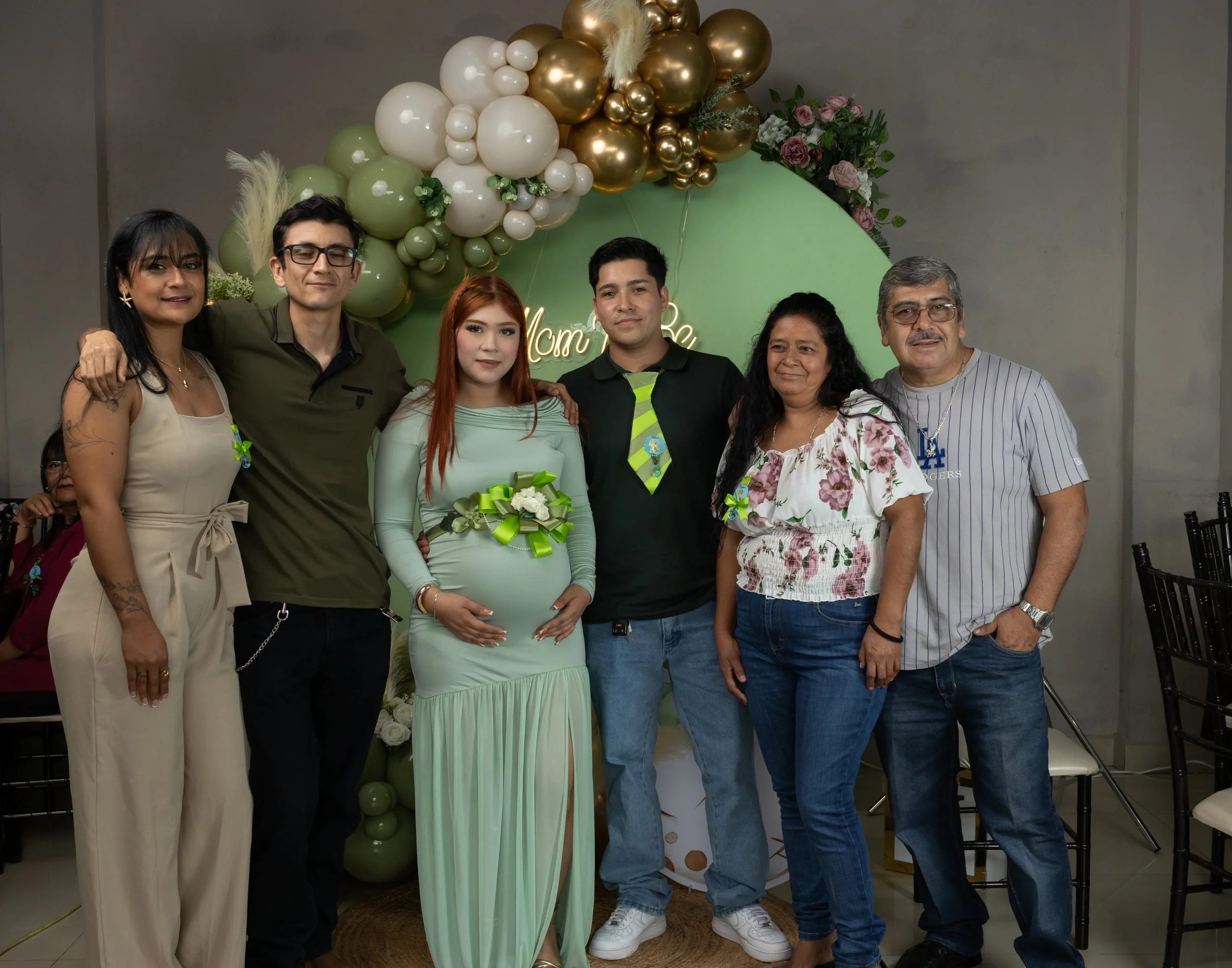 Guiamos a la familia para una pose natural frente al set principal. La iluminación equilibrada y los tonos coordinados refuerzan unidad y apoyo en esta etapa.