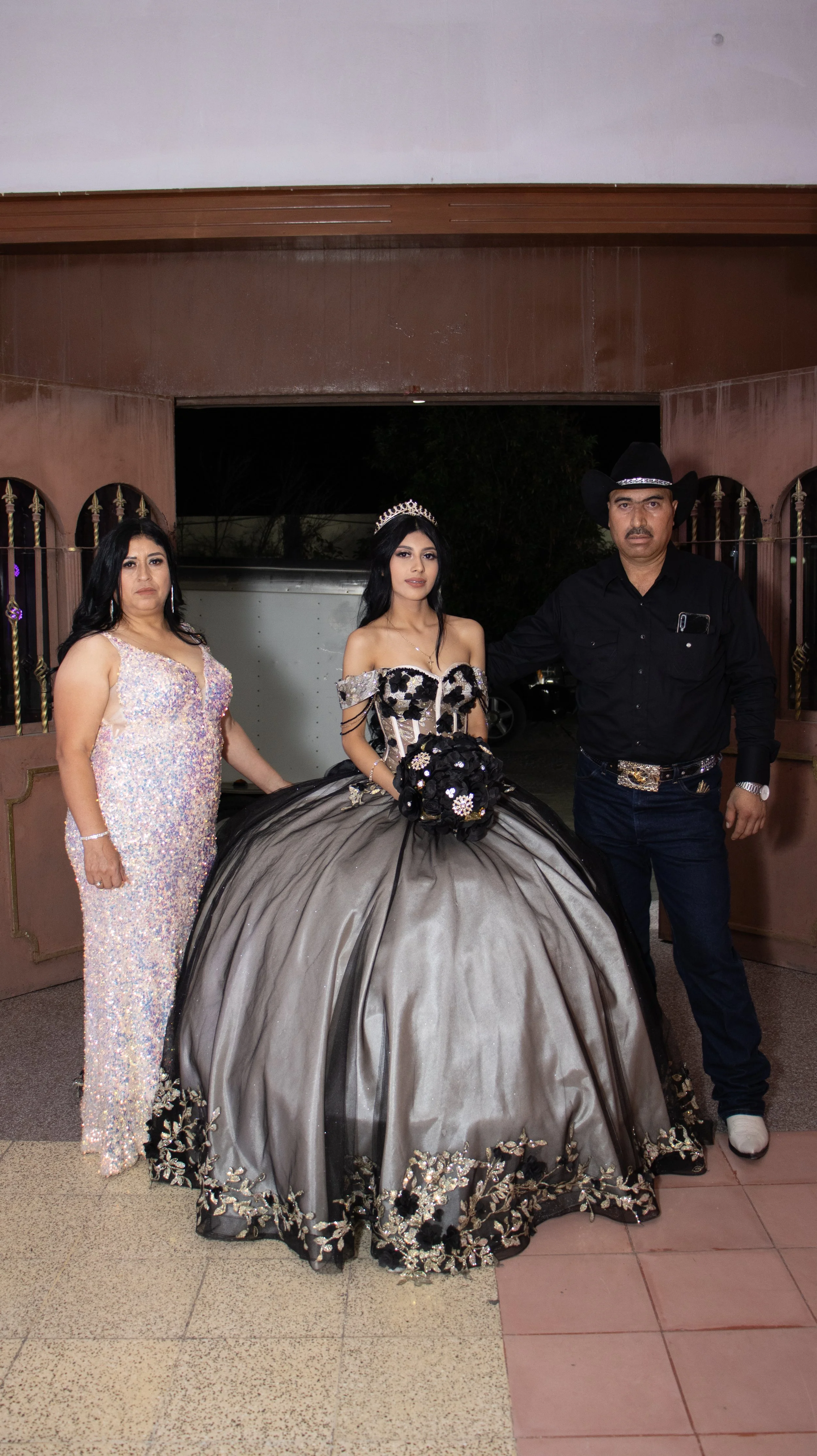 Iluminación frontal suave y pose clásica para un retrato formal. Centramos a la quinceañera y equilibramos a los padres a cada lado, cuidando texturas del vestido y brillo de accesorios para un recuerdo de portada.