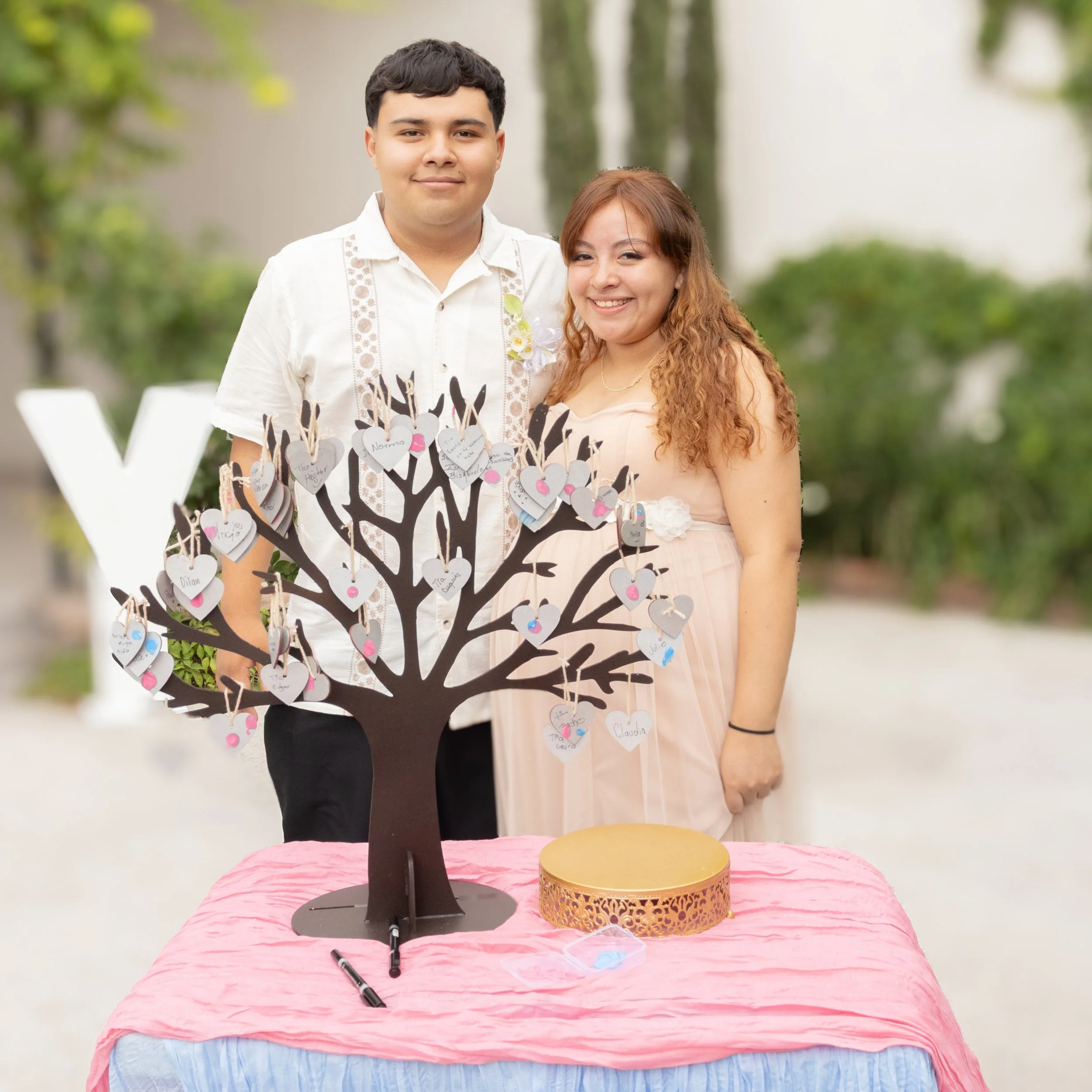 Realizamos un retrato cercano con profundidad de campo corta para resaltar a la pareja y el árbol de huellas que destaca la probabilidad del sexo del bebe, La composición deja el fondo suave y equilibrado, dando prioridad a las sonrisas y al detalle 