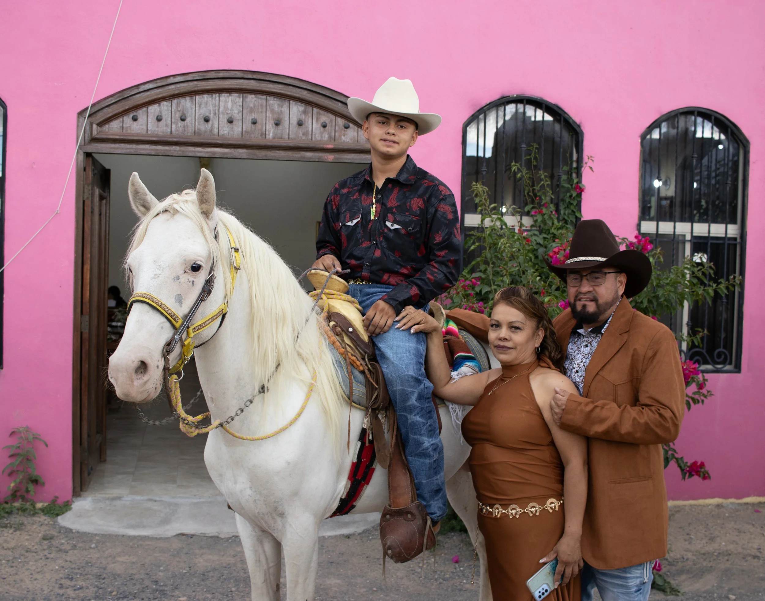 Composición ambiental frente a la iglesia rosa para un contraste vibrante. Integramos al caballo y la familia en una pose natural, manteniendo nítidos los detalles de la montura y las flores del entorno.