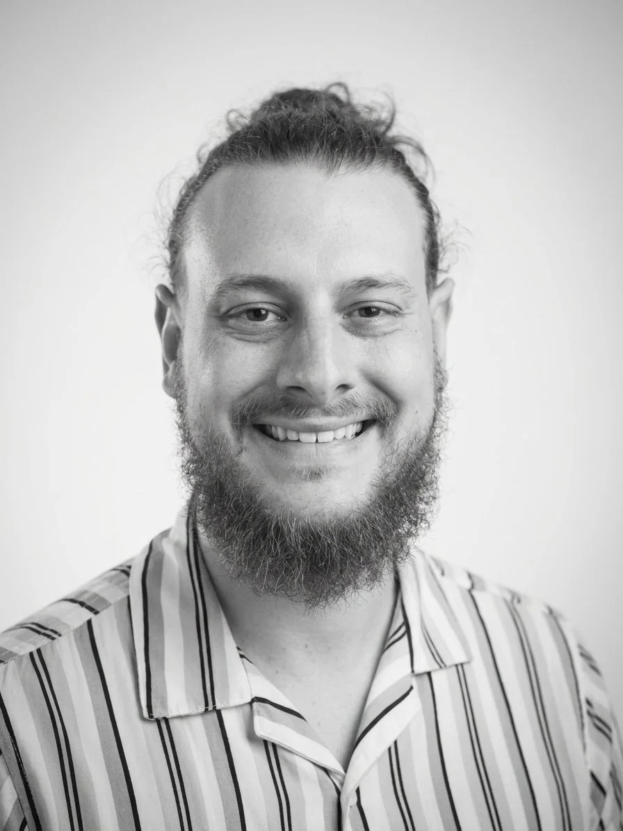 Black and white portrait of a young man with short hair, smiling, wearing a collared shirt, against a plain light background.