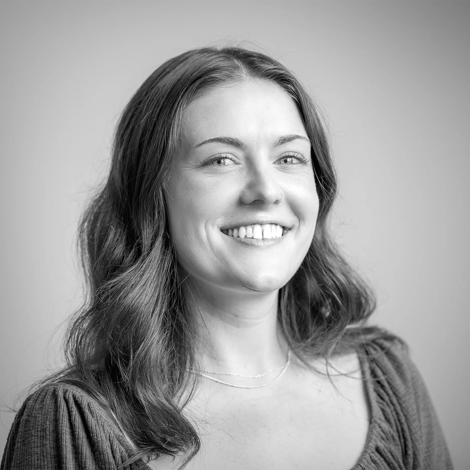 Black and white portrait of a smiling woman with long wavy hair, wearing hoop earrings and a V-neck top, against a plain background.