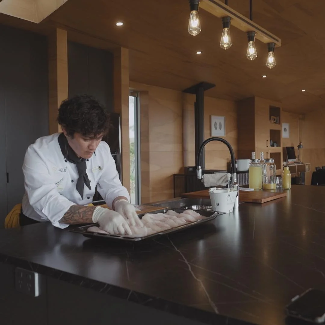 A chef in a white coat and black tie preparing raw fish on a countertop in a modern kitchen.