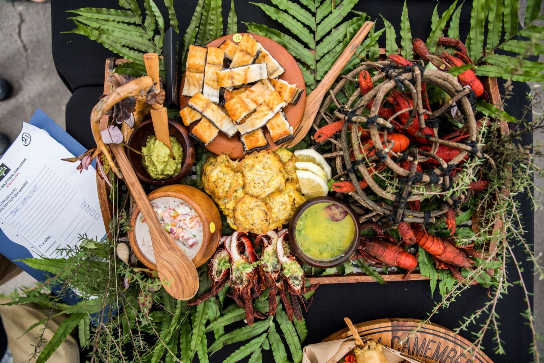 A tray of assorted seafood, including sushi, lobster, grilled fish, and dipping sauces, garnished with green leaves and herbs.