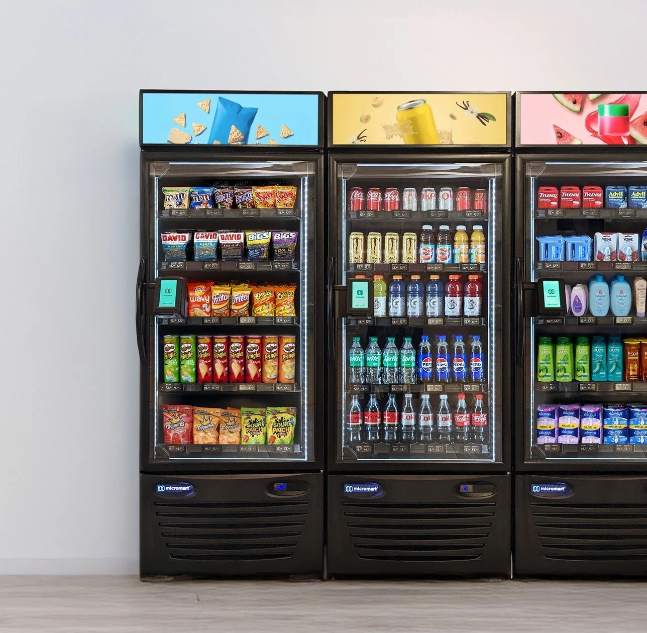Three vending machines filled with snacks, drinks, and beverages, positioned against a white wall.