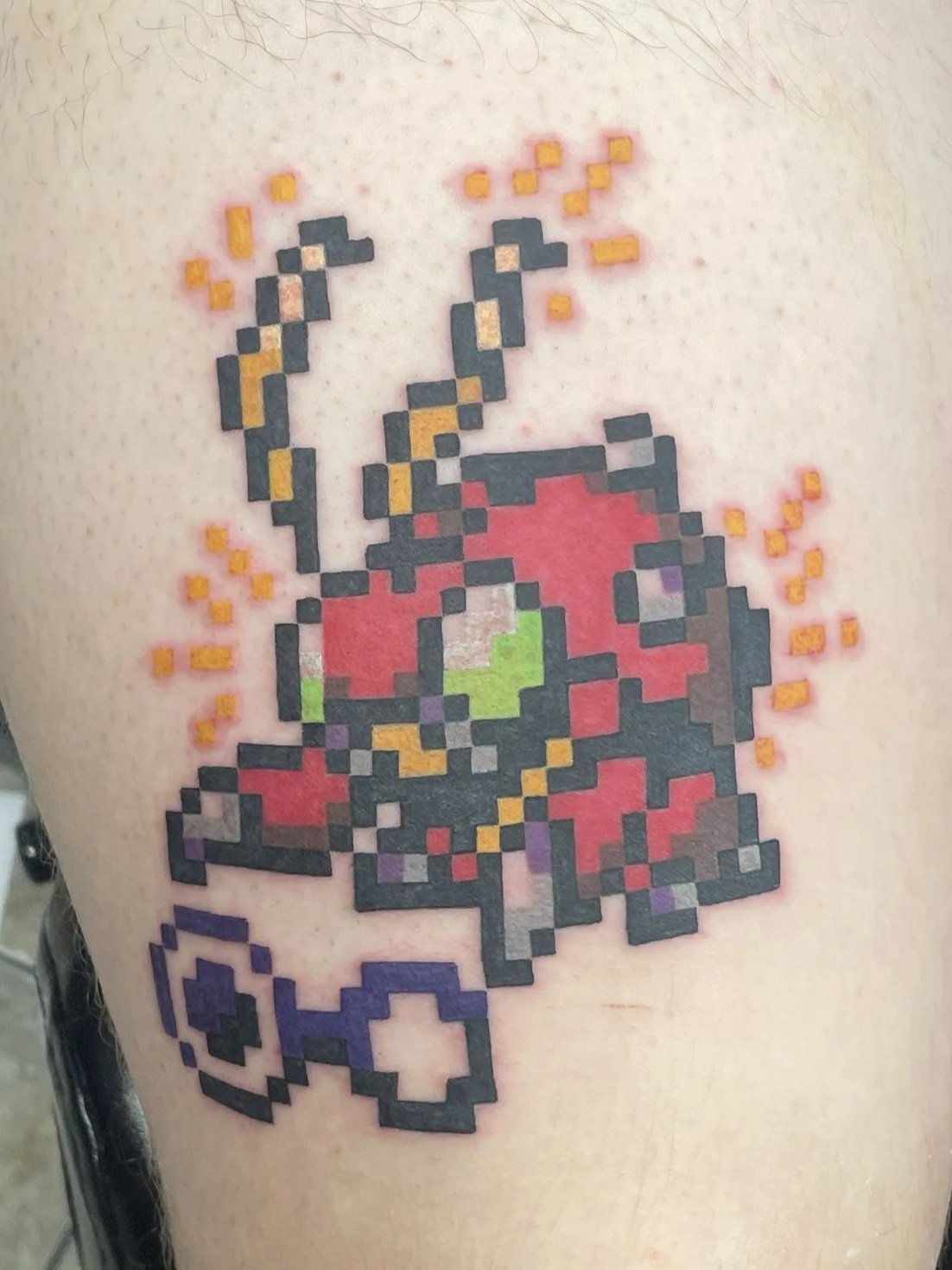 Pixel art style tattoo of a Digimon, surrounded by orange sparks, tattooed by Zing Phelps, in Cedar Rapids, Iowa