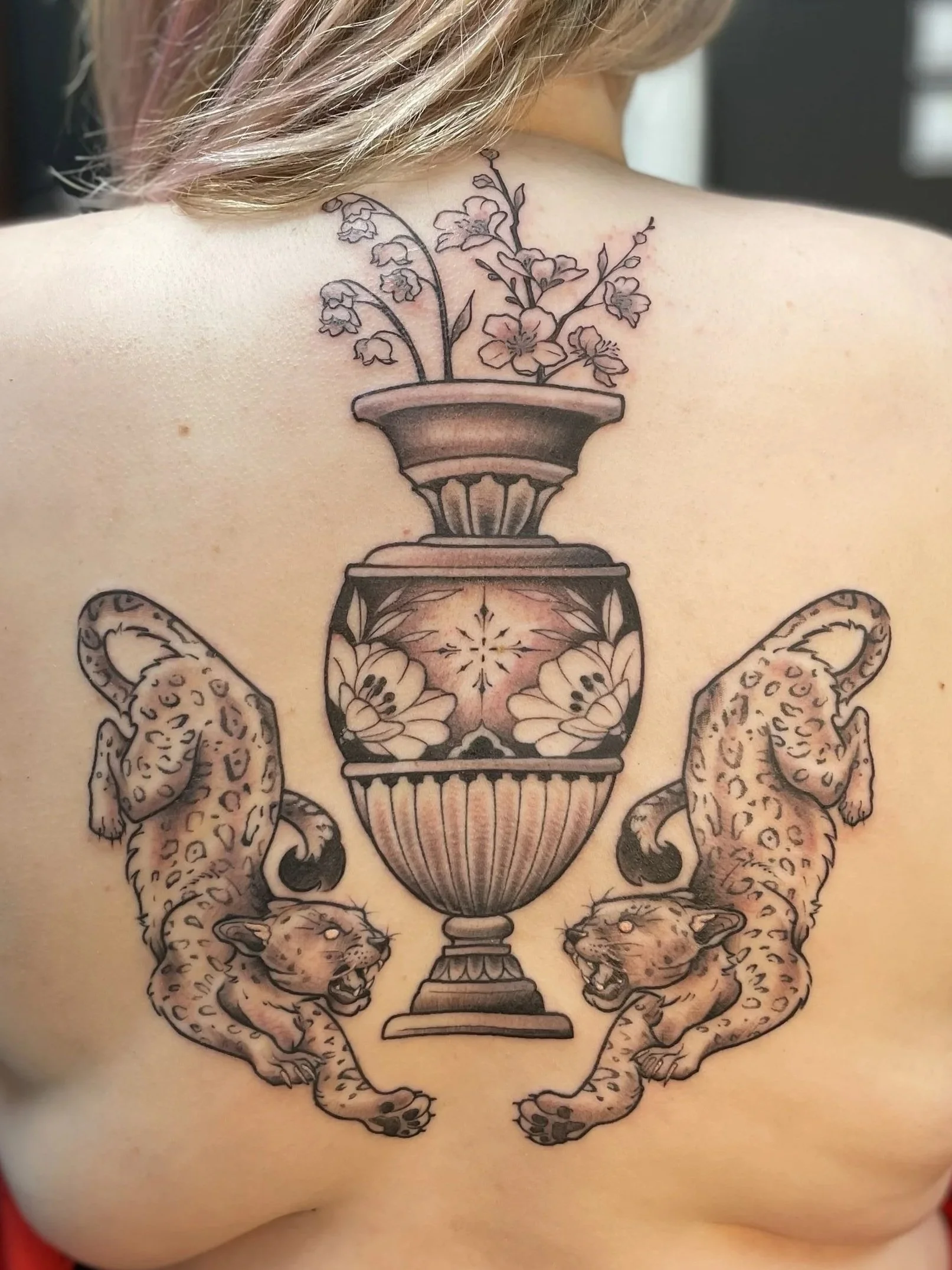 Tattoo on person's back of two leopards facing a decorative urn with flowers and branches, created by Zing Phelps, in Cedar Rapids, Iowa