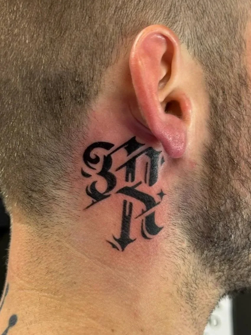 Tattoo behind the ear with black gothic-style lettering, tattooed by Zing Phelps, in Cedar Rapids, Iowa