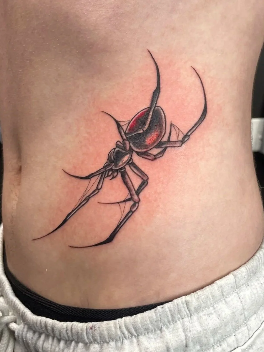 Tattoo of a detailed black and red spider on the person's stomach, tattooed by Zing Phelps, in Cedar Rapids, Iowa
