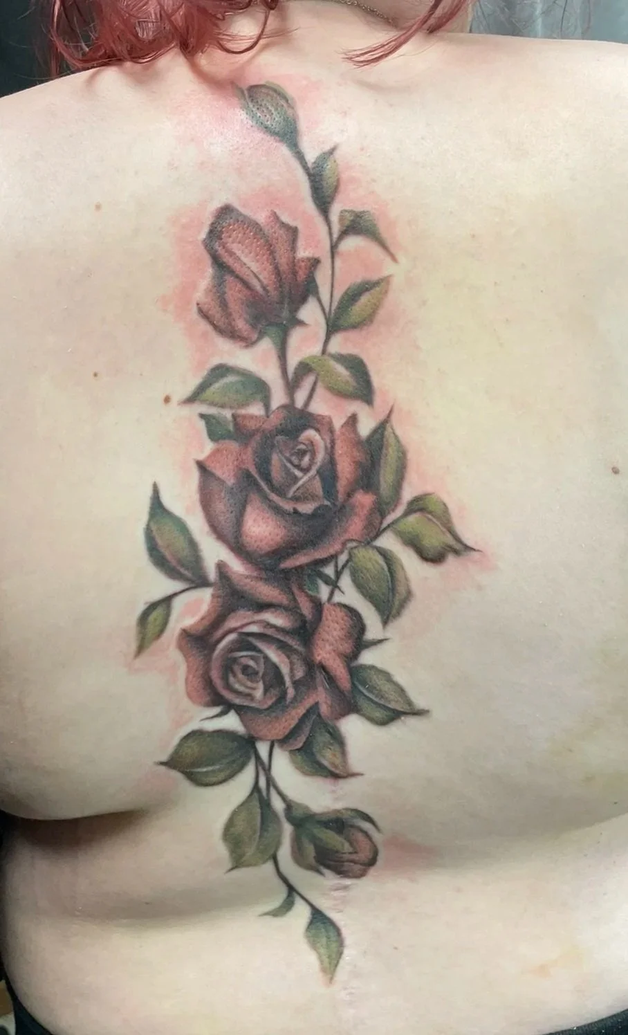 A color realistic floral tattoo of roses and leaves running vertically down the person's back, tattooed by Zing Phelps, in Cedar Rapids, Iowa