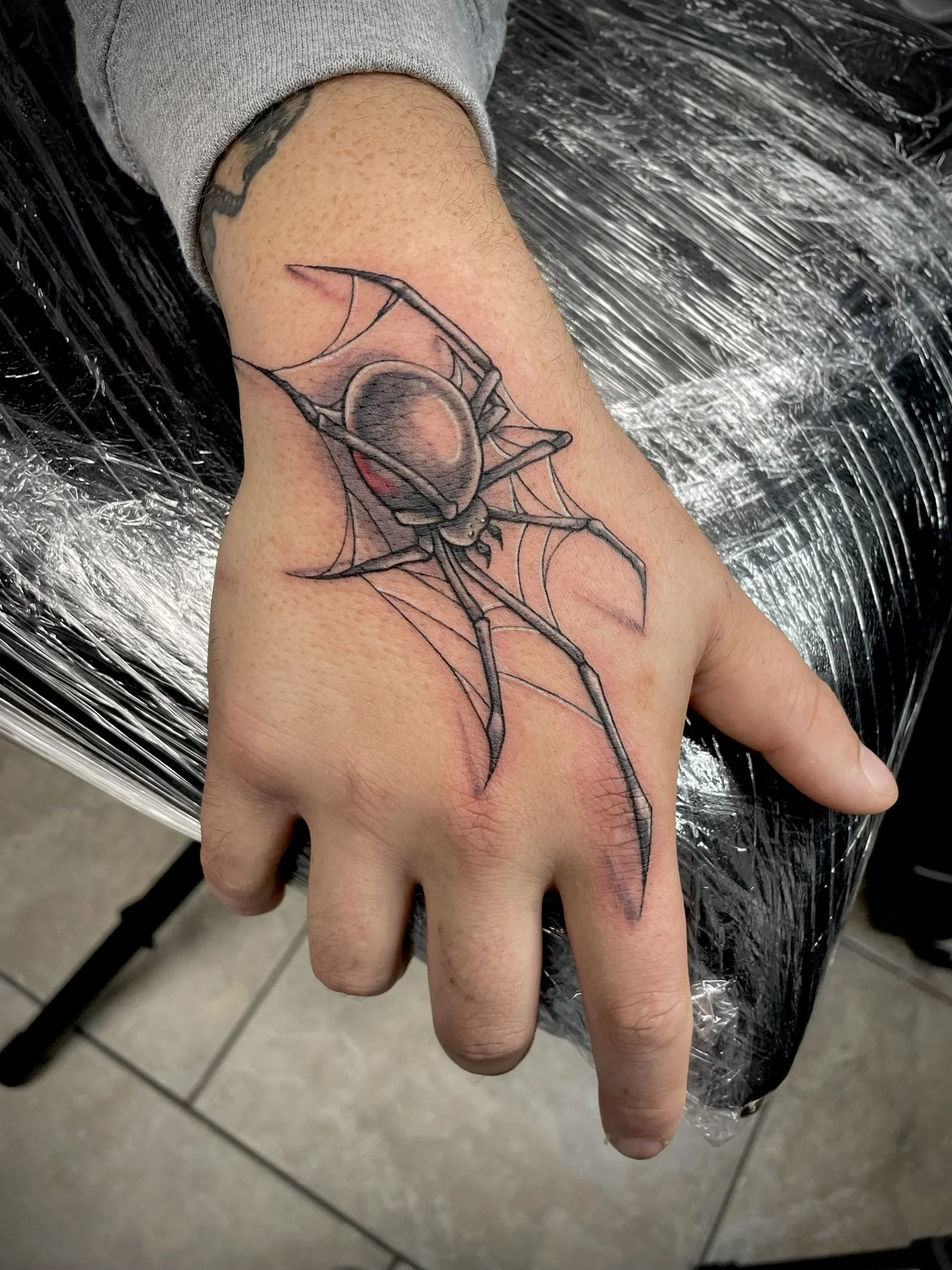 A tattoo of a spider with cobwebs on a person's hand, tattooed by Zing Phelps, in Cedar Rapids, Iowa