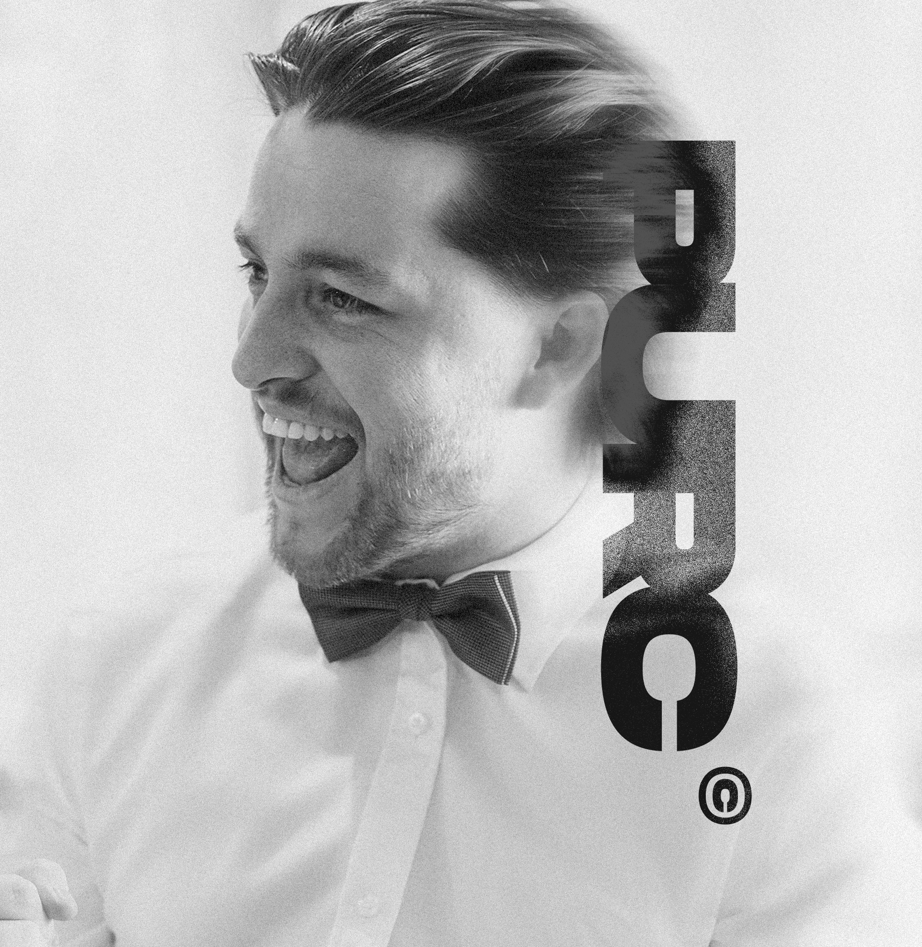 Black and white photo of a smiling man wearing a bow tie and white shirt, with the word "GUESS" vertically overlayed on the right side.
