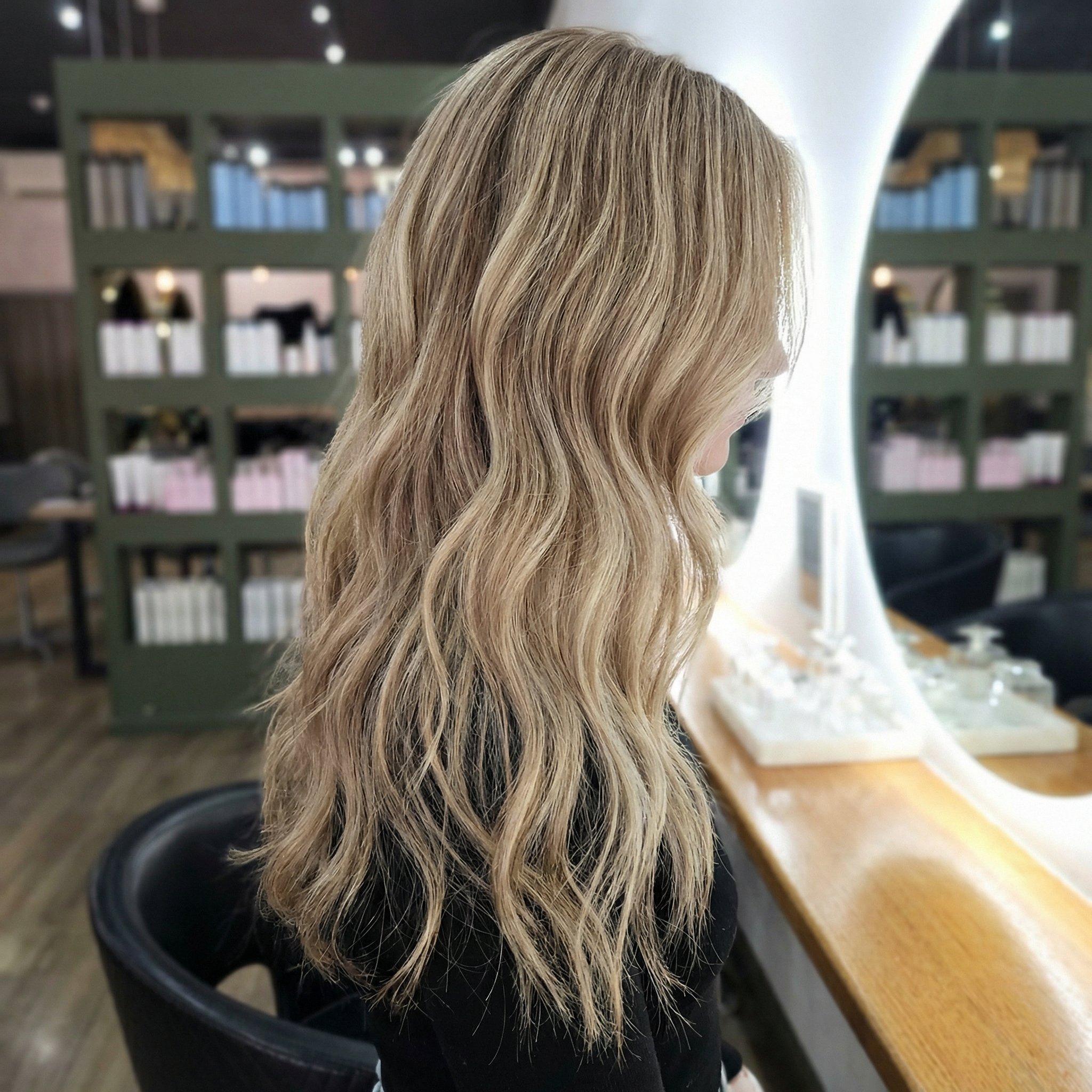 Woman with long, wavy blonde hair sitting at a salon station in a hair salon.