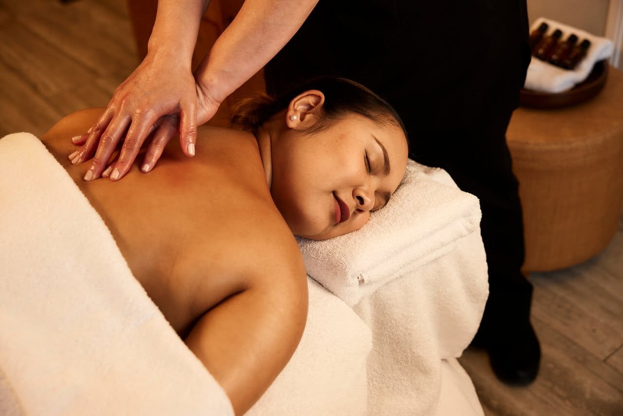 A woman receives a back massage while lying face down on a massage table with a white towel.