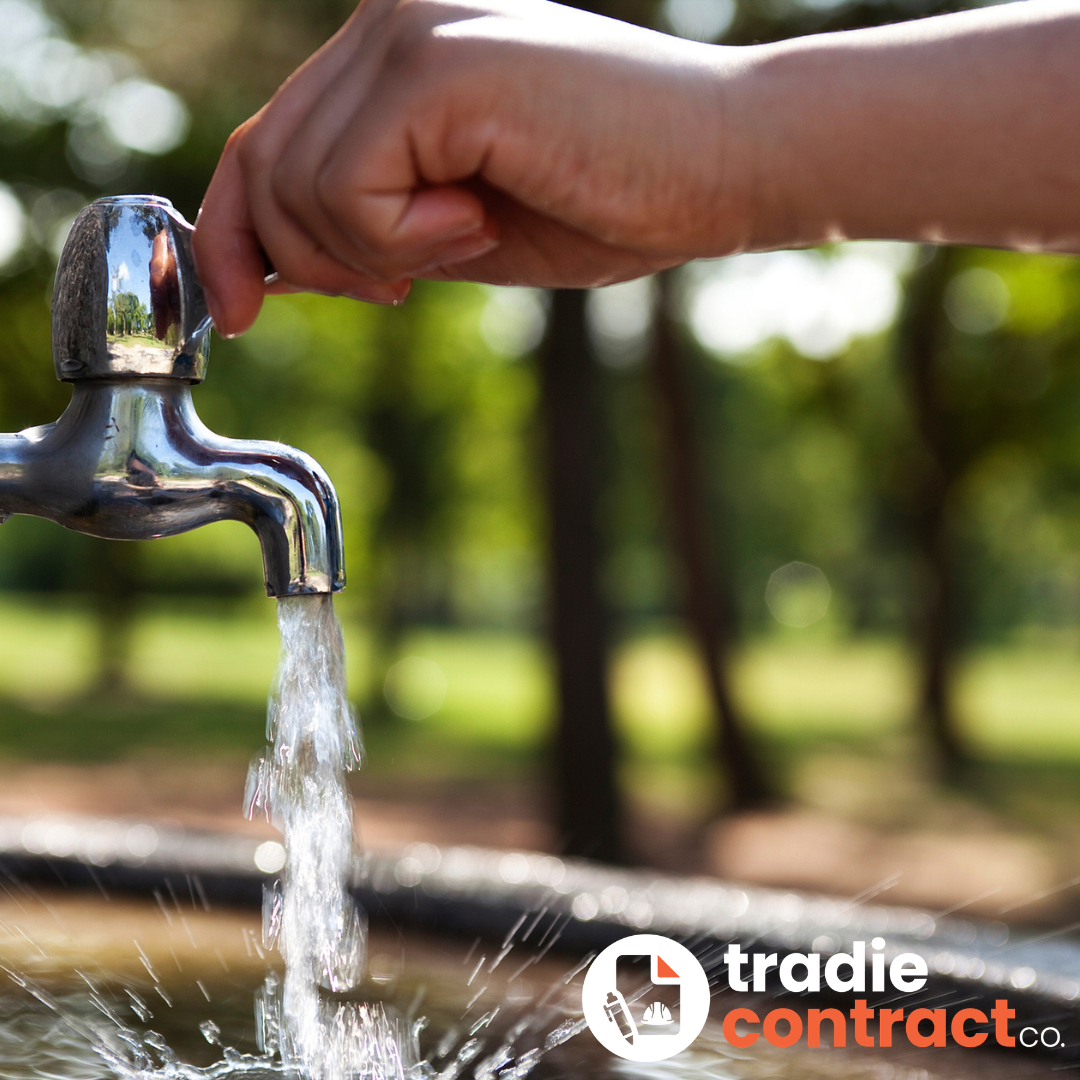 A person filling a cup with water from a silver faucet outdoors, with trees in the background.