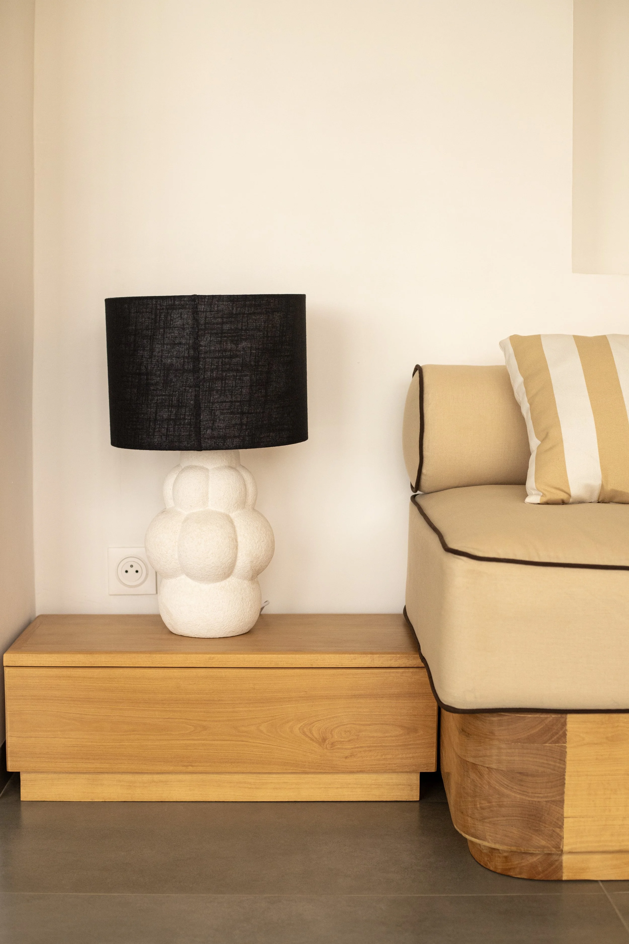 Lampe de table noire avec base en forme de boules blanches sur une table en bois à côté d'un canapé beige avec coussin rayé blanc et beige.