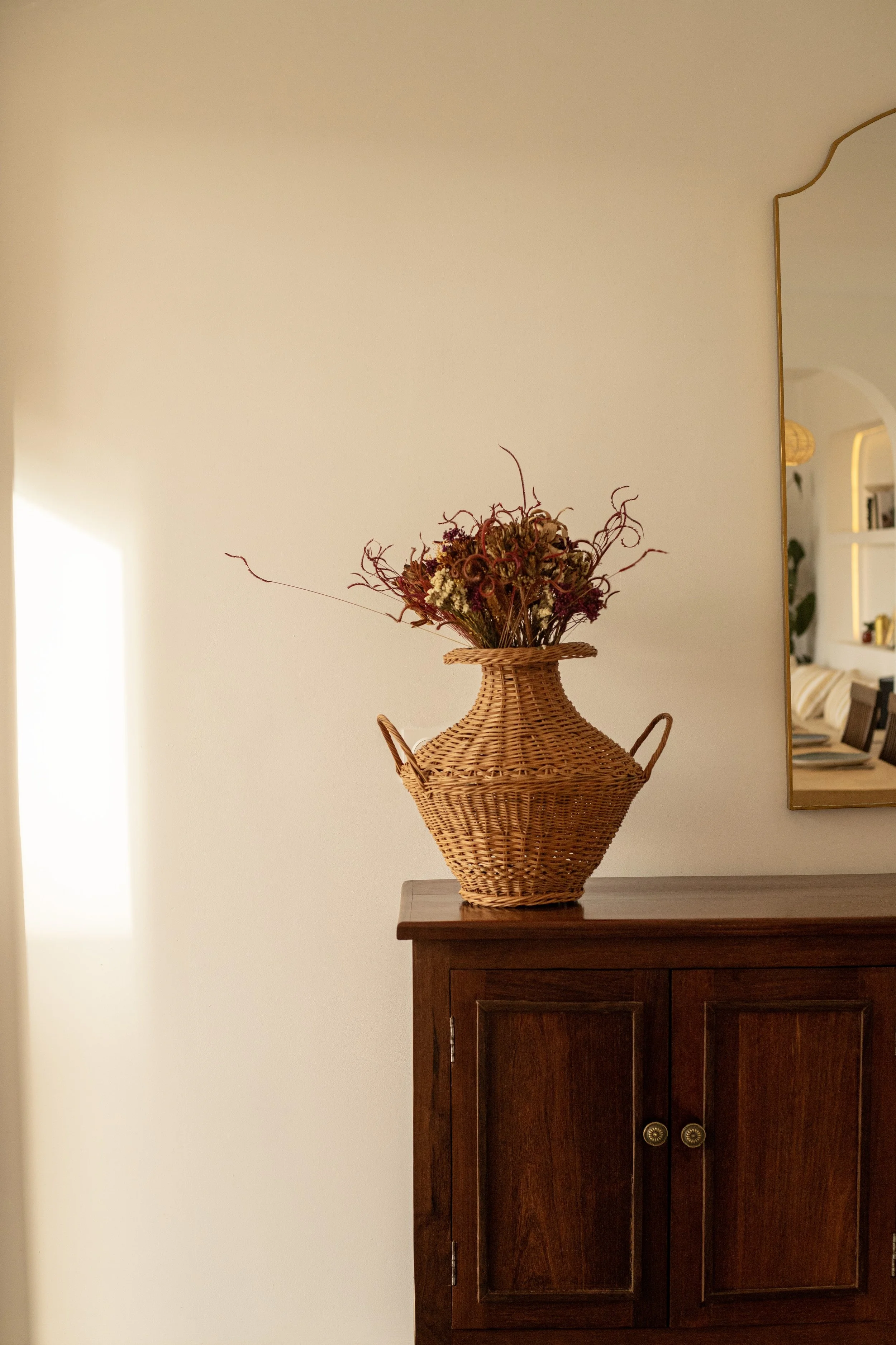 Vase en rotin avec des fleurs séchées sur une armoire en bois.