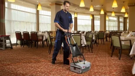 A man cleaning the carpet in a restaurant with a carpet-cleaning machine.