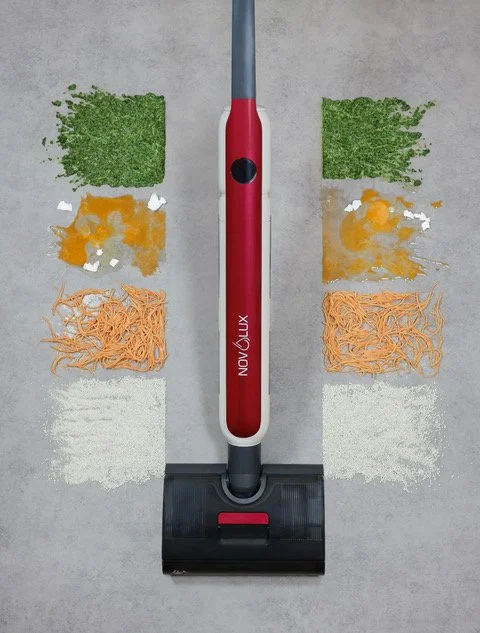 A vacuum cleaner with piles of chopped vegetables: kale, carrots, zucchini, and zucchini slices, arranged around it on a gray floor.