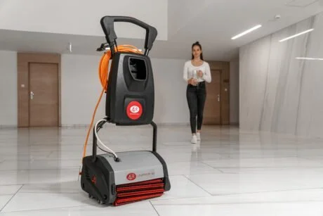 A woman walking in a modern, empty lobby with a large industrial floor cleaning machine in the foreground.