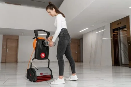A woman cleaning a floor with a black and red carpet cleaner in a modern building lobby.