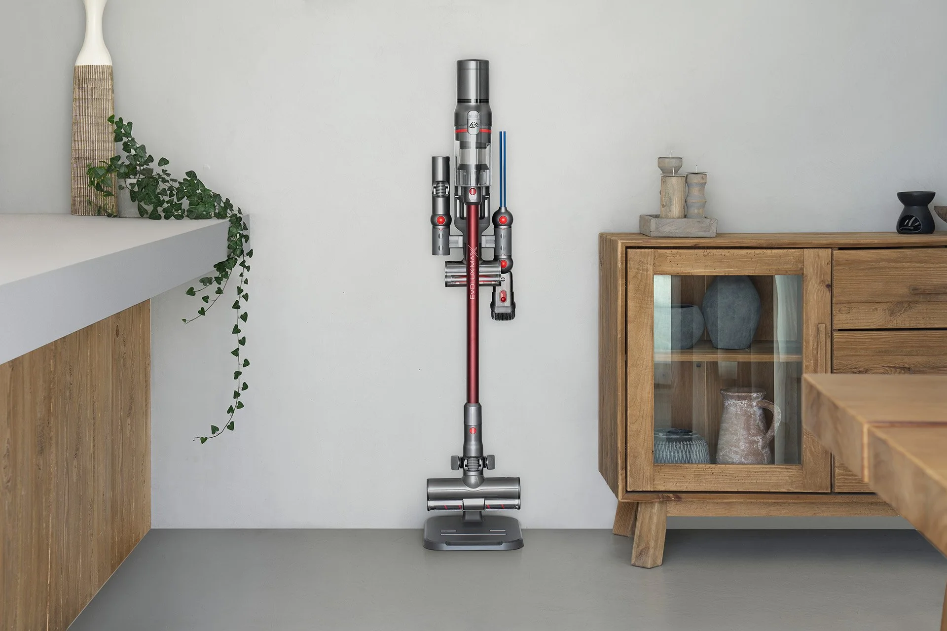 A cordless vacuum cleaner mounted on a white wall in a modern, minimalist room with wooden furniture and decorative vases.