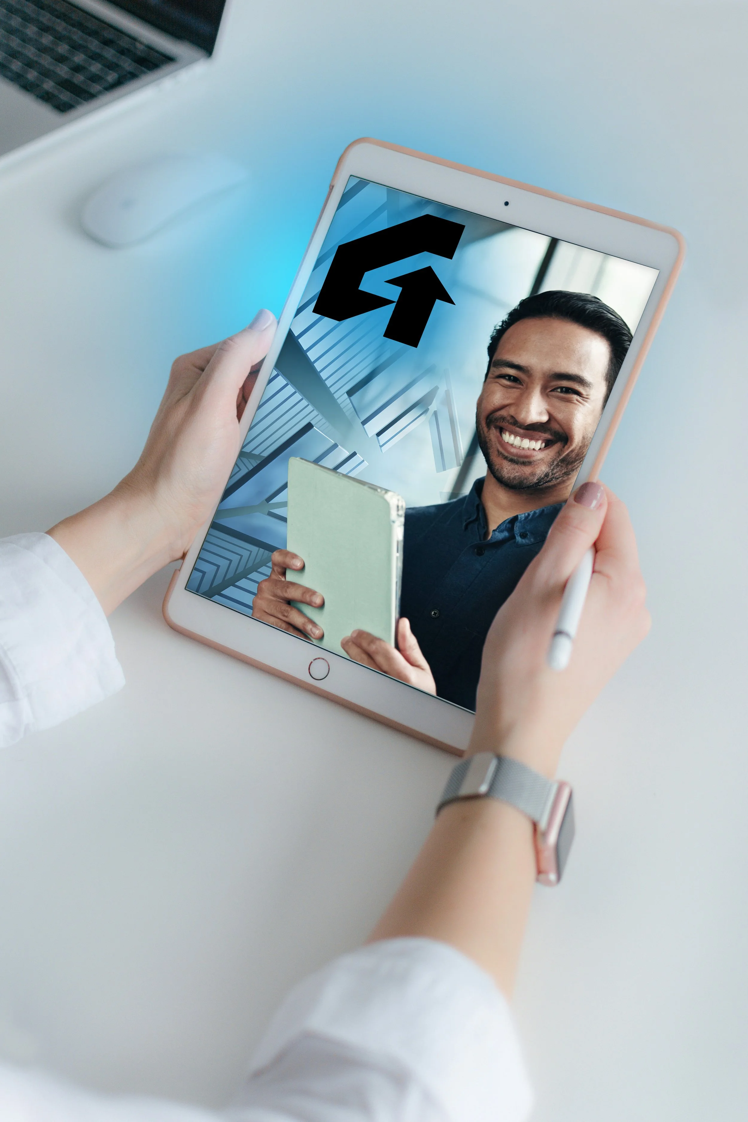 Person taking a selfie with a tablet, showing a smiling man holding a notebook, with a large black arrow pointing up on the tablet screen.