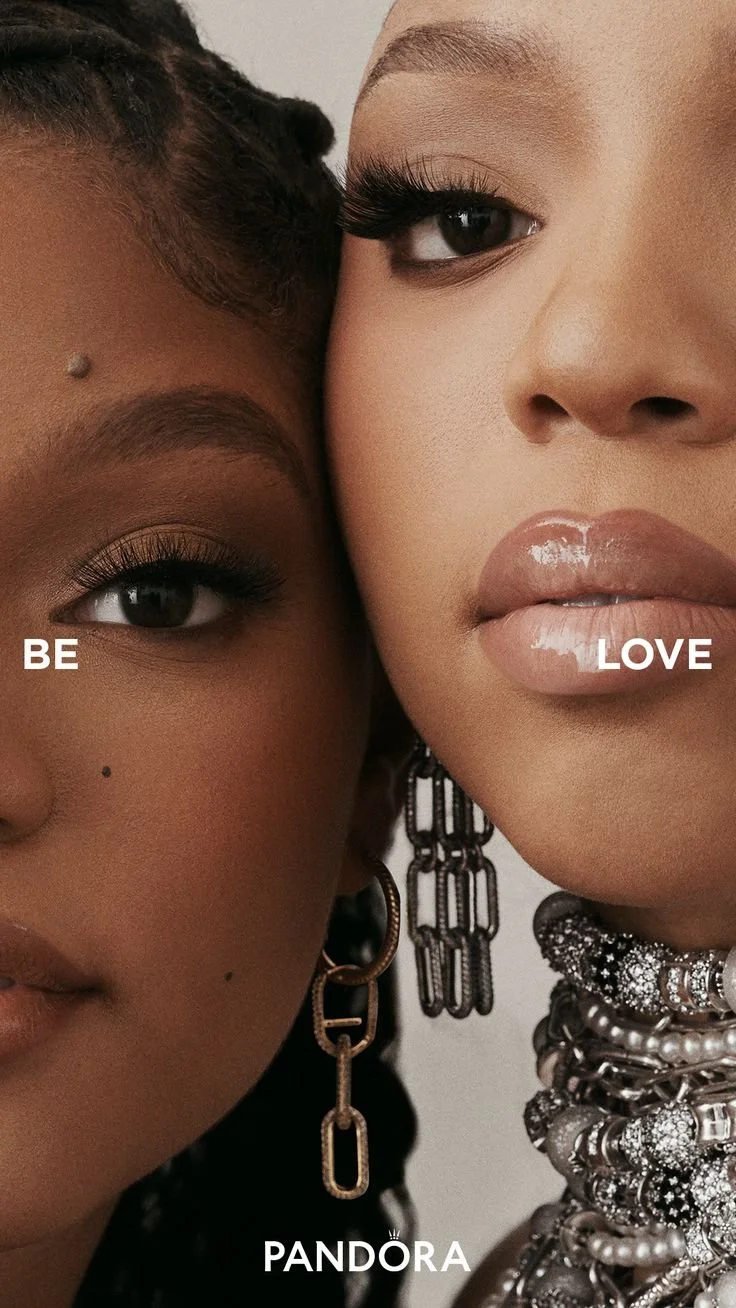Close-up of two women with makeup and jewelry, with words 'BE', 'LOVE', and 'PANDORA' overlayed.