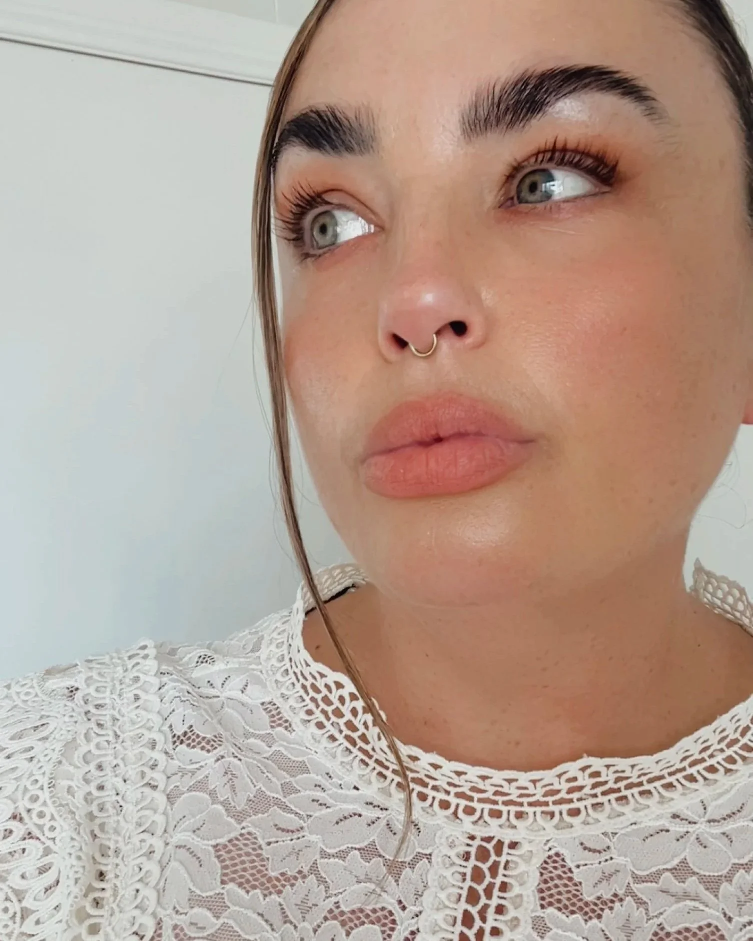 Close-up of Clinic Founder Melissa White's face with blue eyes, dark eyebrows, long eyelashes, and a septum piercing, wearing a white lace top.