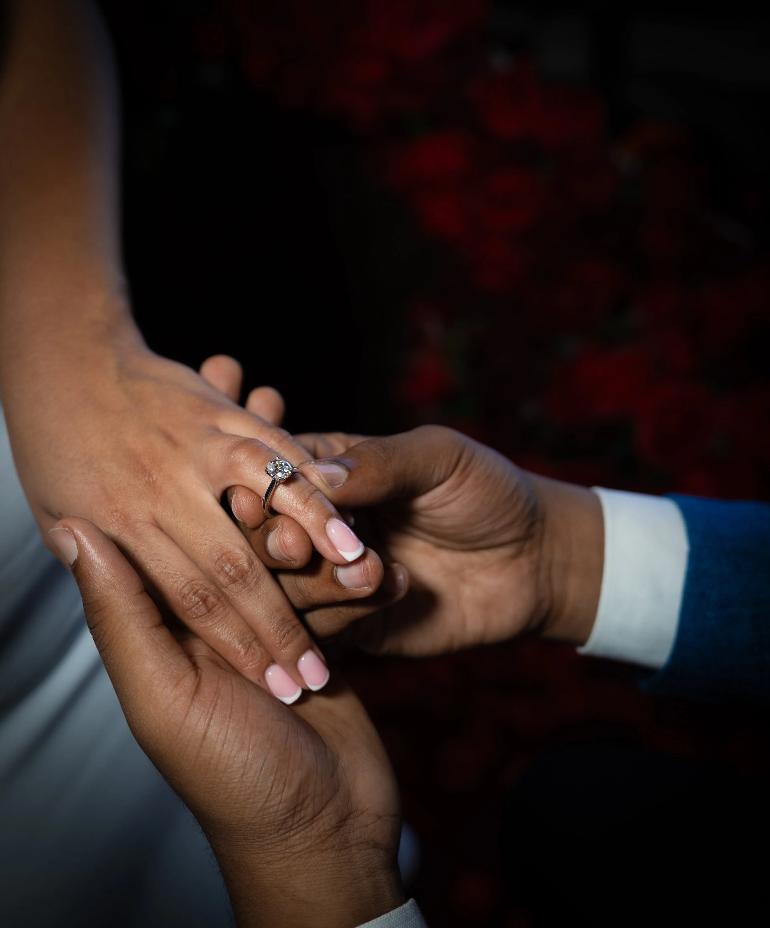 A person with darker skin receiving a ring on their finger from another person with lighter skin during a wedding or engagement ceremony.