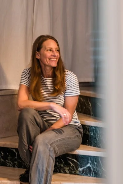 Eine lachende Frau sitzt auf einer Treppe, trägt ein gestreiftes T-Shirt und Jeans.