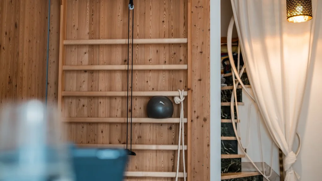 Blick auf eine Sprossenwand mit einem dunkelgrauen Medizinball und einem Seil.