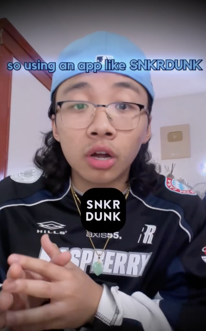 A young man with glasses, wearing a blue cap and a sports jacket, speaking in a room with a wooden door and a YouTube plaque on the wall. There is text overlay about using an app called SNKRDUNK.