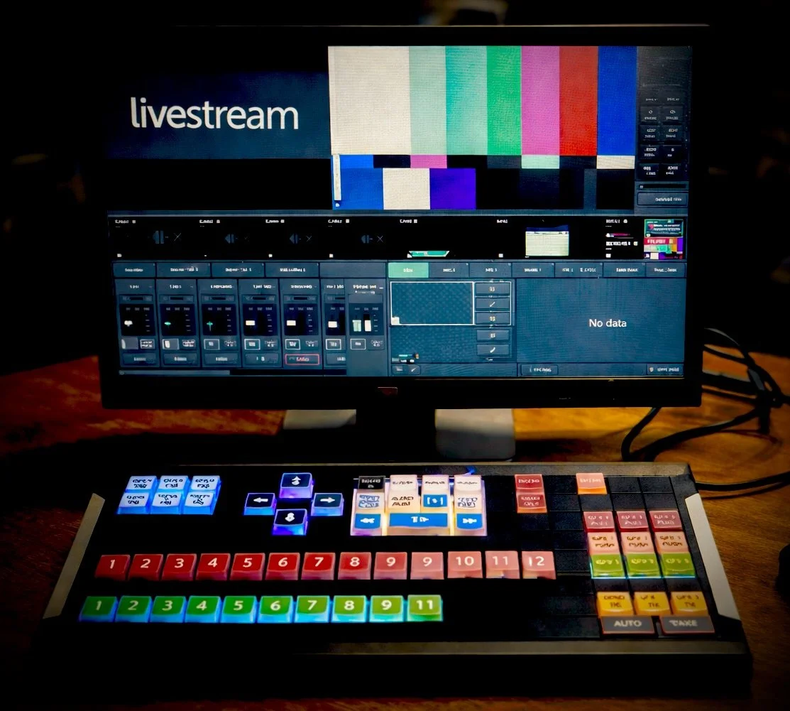 Television screen displaying a color test pattern and Livestream graphics, with a video switcher console in the foreground showing various colored buttons and controls.